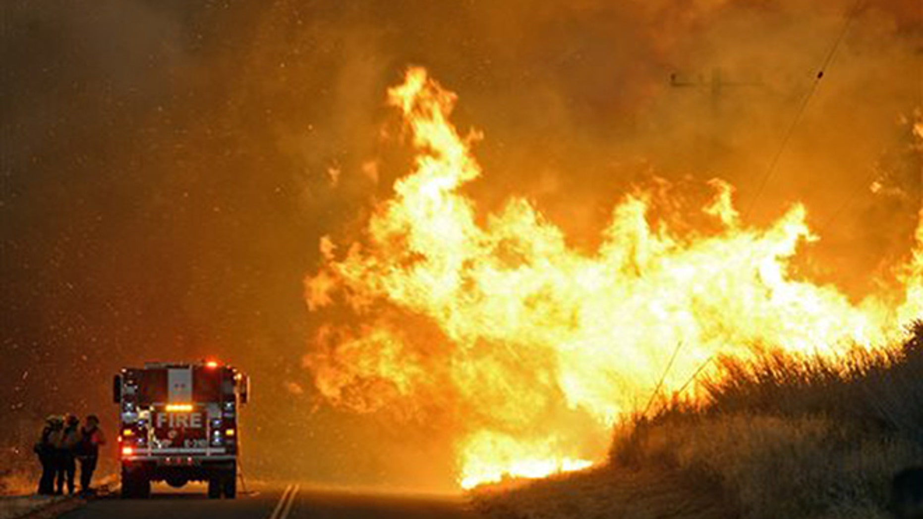 Firefighters from the Lompoc City Fire Department take shelter behind their engine Thursday, June 16, 2016, as wind driven flames advance from the Sherpa Fire. The flames were crossing Calle Real near El Capitan State Park in Santa Barbara County. (Mike Eliason/Santa Barbara County Fire Department via AP)