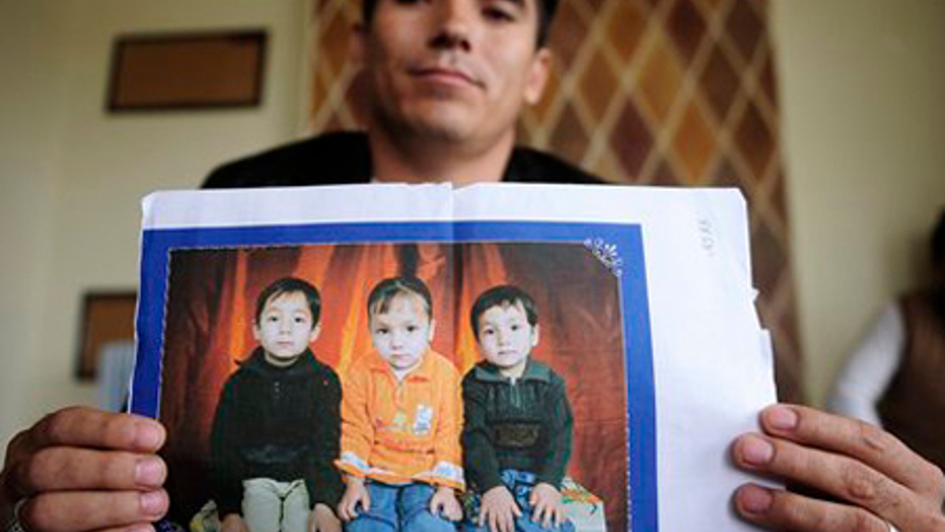 Ali Khosh Razaee holds pictures of his three young children at a house in an Adelaide, Australia, suburb.