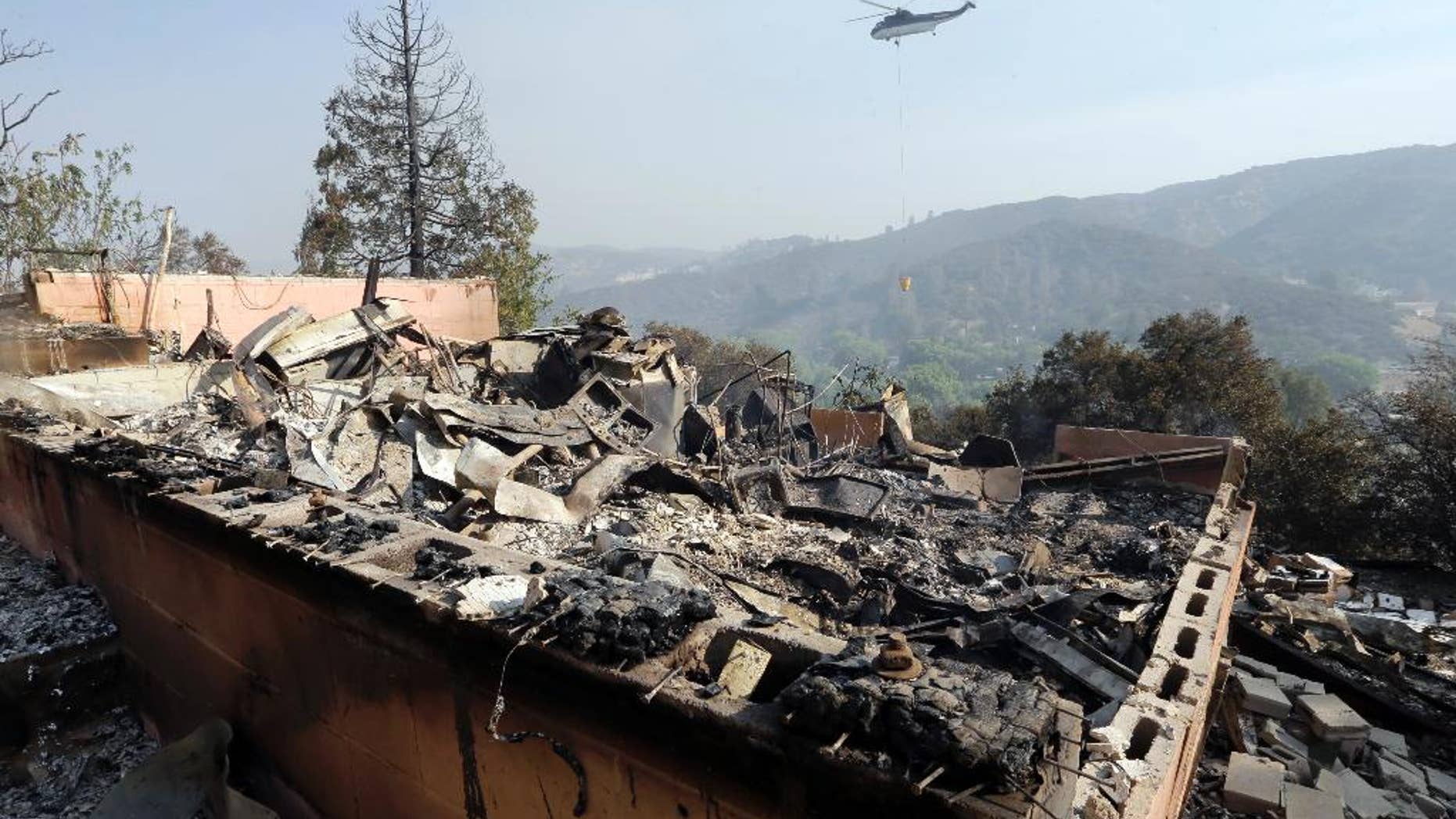 A firefighting helicopter carries a large water bucket behind a home that has been destroyed by a fire in Lake Hughes, Calif., in this June 2, 2013, photo.