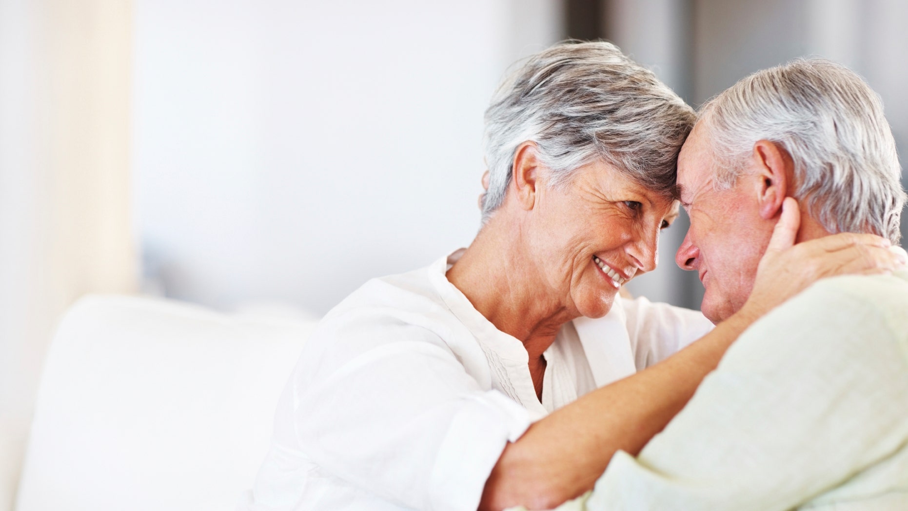Romantic mature couple smiling head to head while sitting on couch