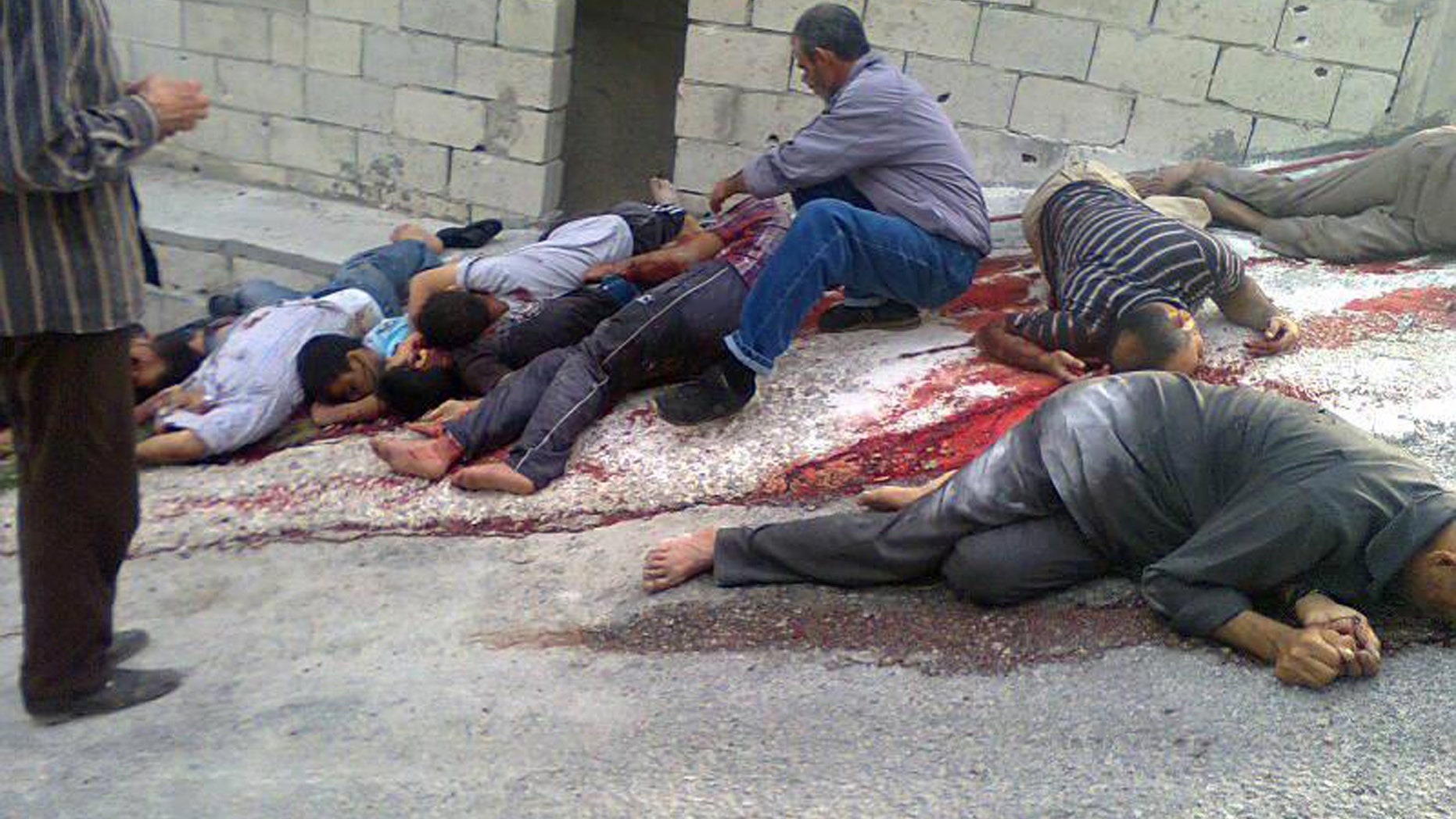In this citizen journalism image released on Thursday, May 2, 2013 by a group that calls itself The Syrian Revolution Against Bashar Assad, which has been authenticated based on its contents and other AP reporting, a Syrian man, center, identifies dead bodies, who were killed according to activists by Syrian forces loyal to Bashar Assad, in Bayda village, in the mountains outside the coastal city of Banias, Syria. Syria's main opposition group on Friday accused President Bashar Assad's regime of committing a "large-scale massacre" in a Sunni village near the Mediterranean coast, killing scores of people, according to activists. (AP Photo/The Syrian Revolution Against Bashar Assad)