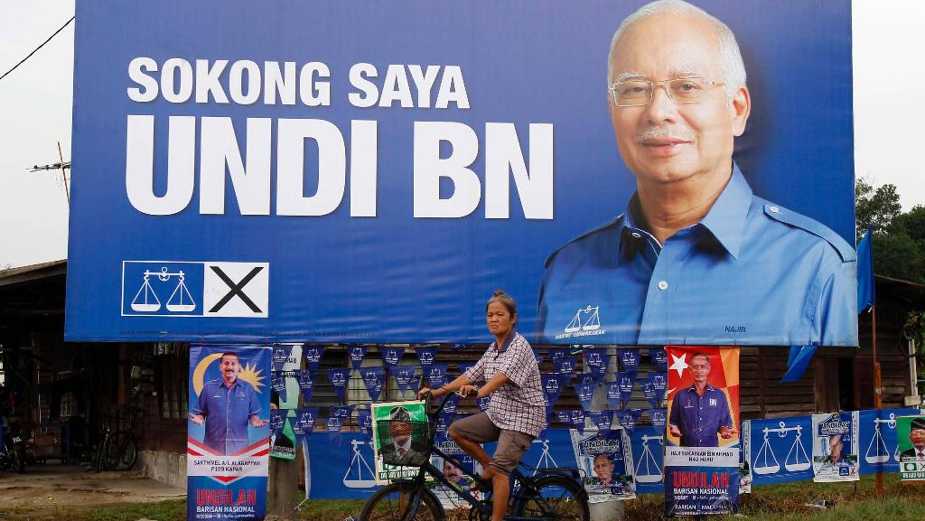 FILE - In this May 3, 2013 file photo, a Malaysian ethnic Chinese woman rides past a billboard of Malaysia's ruling National Front coalition with a portrait of Prime Minister Najib Razak which translates "I vote for National Front coalition" ahead of the upcoming general elections in Klang, outside Kuala Lumpur, Malaysia. The party of Malaysia's scandal-tainted Prime Minister Najib Razak has won two parliamentary by-elections in a landslide, further strengthening his rule despite corruption allegations. (AP Photo/Lai Seng Sin, File)