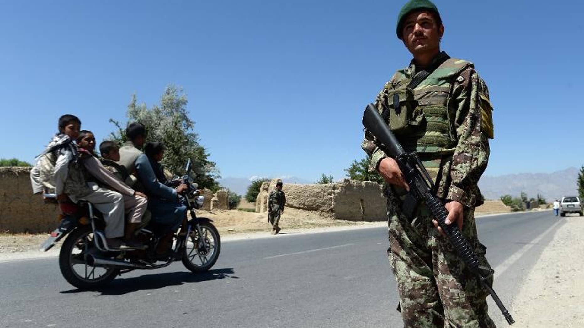 Men on a motorcycle drive past Afghan soldiers on guard outside Bagram military base, 50 kms north of Kabul, on June 19, 2013