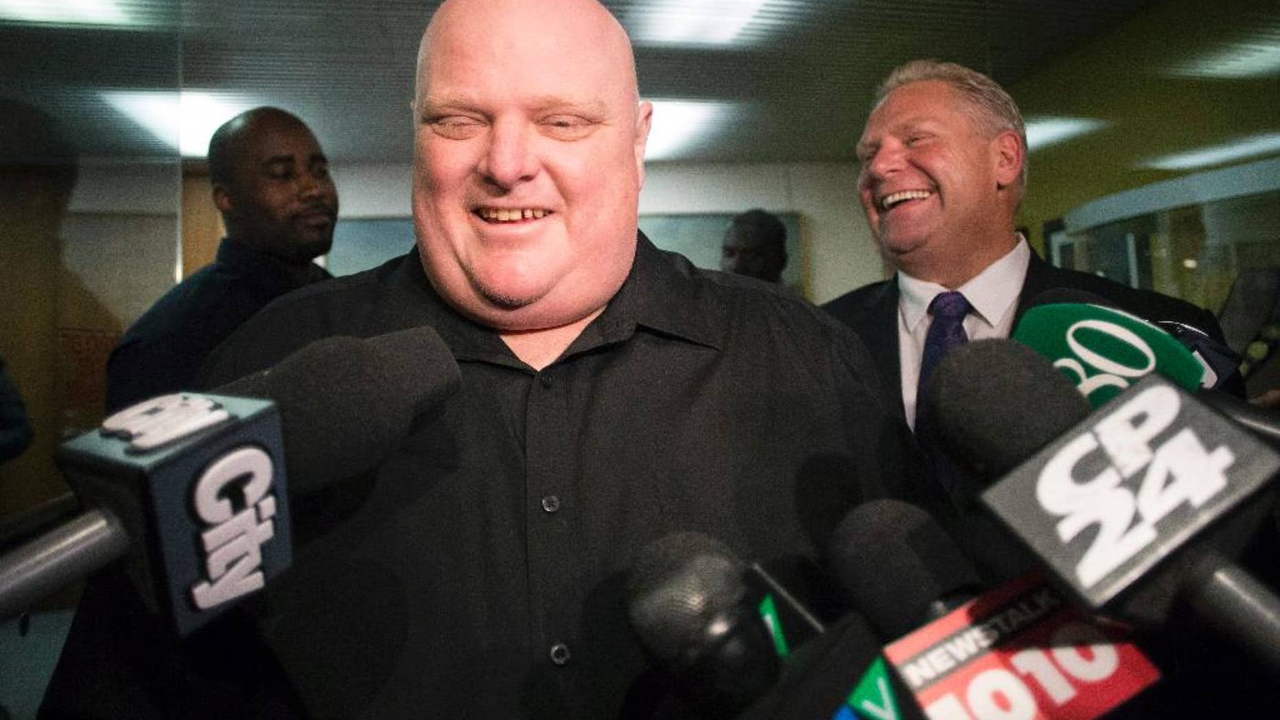 FILE - In this Nov. 21, 2014, file photo, Toronto's outgoing Mayor Rob Ford, front center, stands next to his brother Doug Ford outside his office as he speaks with the media before signing bobblehead dolls in in his likeness in Toronto. The notorious former Toronto mayor and now city councilor is auctioning off some of the memorabilia he has collected over the years. Ford's term was plagued by scandals involving drinking, crack cocaine use and erratic behavior. (AP Photo/The Canadian Press, Chris Young, File)
