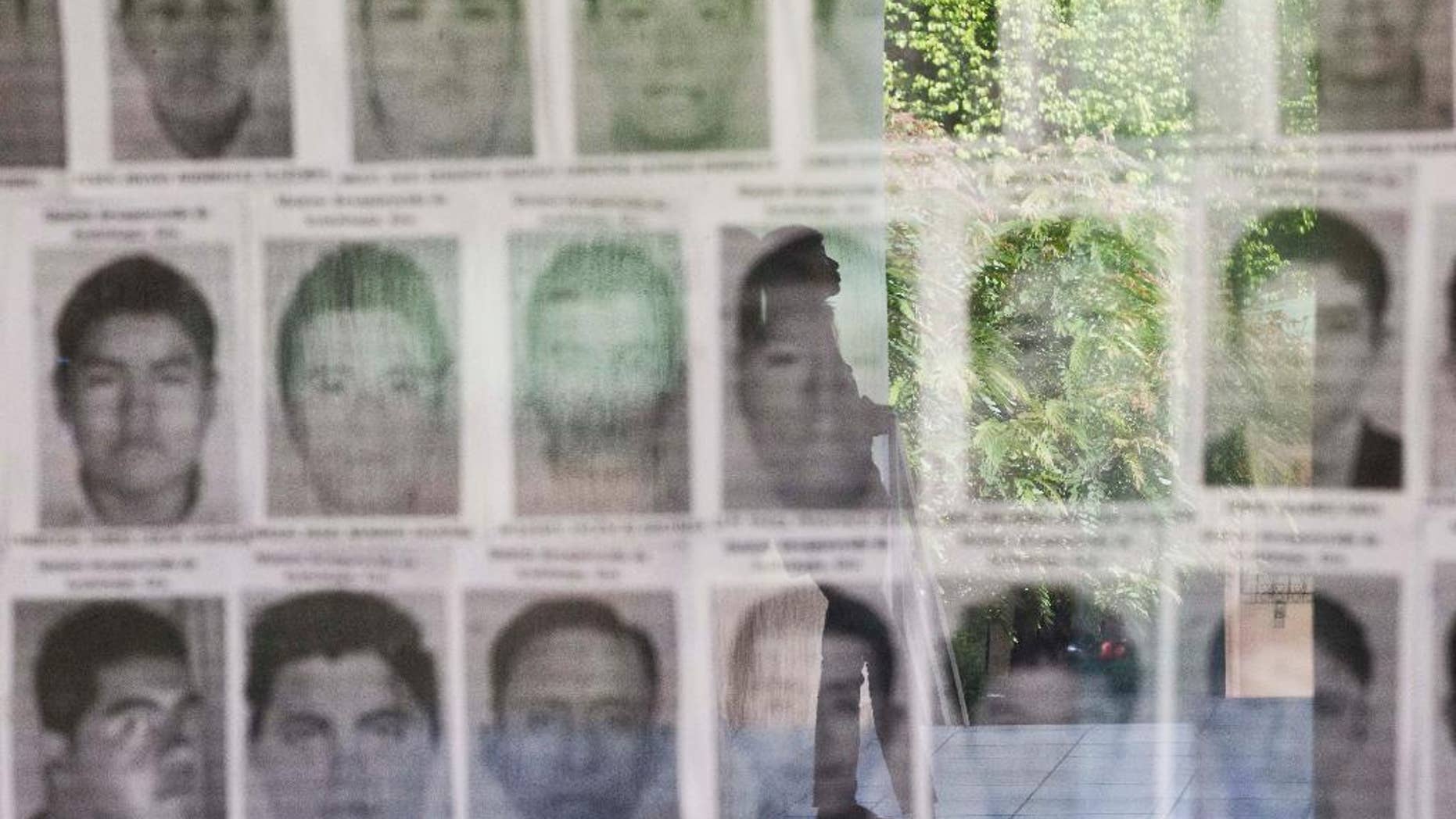 FILE - In this Nov. 18, 2014 file photo, a university student is reflected in a glass display case showing the photos of 43 missing students from the Rural Normal School of Ayotzinapa, Mexico, at the Central American University, UCA, in Managua, Nicaragua. Mexican authorities announced they detained on Friday, Oct. 21, 2016 the former police chief of Iguala where the students disappeared on Sept. 26, 2014. The students were taken by police and have not been heard from since. (AP Photo/Esteban Felix, File)