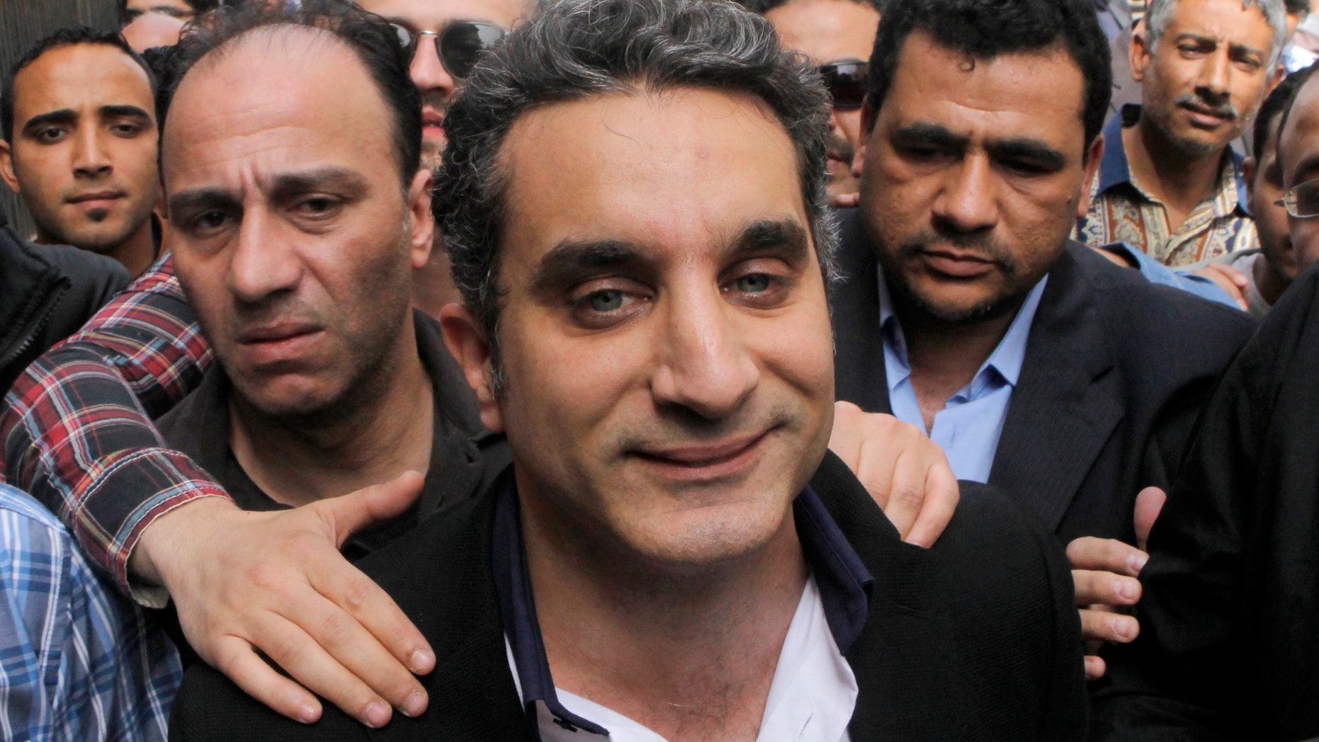 FILE - In this Sunday, March 31, 2013 file photo, a bodyguard secures popular Egyptian television satirist Bassem Youssef, who has come to be known as Egypt's Jon Stewart, as he enters Egypt's state prosecutors office to face accusations of insulting Islam and the country's Islamist leader in Cairo, Egypt. Egypt's state Investment Authority said Tuesday, April 2, 2013 it will revoke the license of a private TV station that airs a popular satirist if he does not stop the use of "unacceptable and offensive" language. The warning comes two days after the satirist, Youssef, was questioned by prosecutors over accusations that he insulted Islamist President Mohammed Morsi and Islam, and a day after the U.S. criticized the Egyptian government for a "disturbing trend" of growing restrictions on freedom of expression. (AP Photo/Amr Nabil, File)