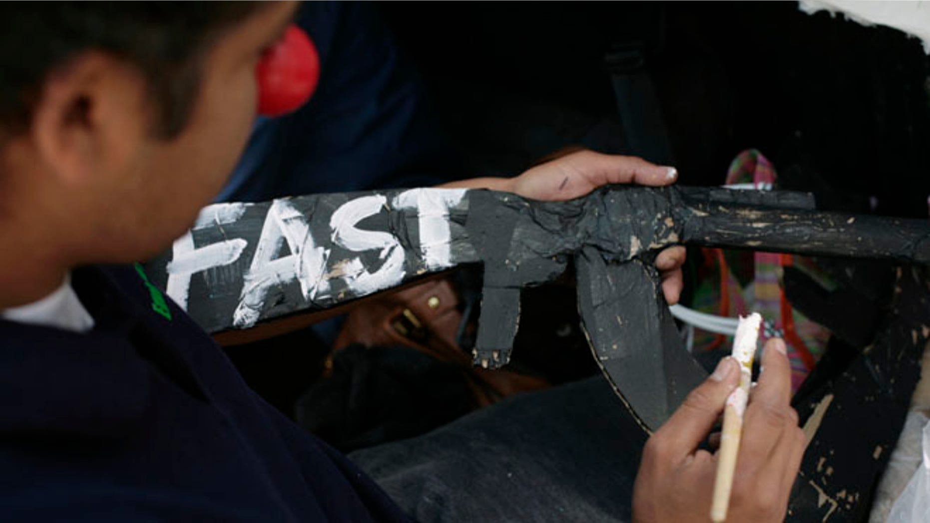 FILE: October 14, 2011: A man writes "Fast" -- in reference to Operation Fast and Furious -- on a paper mache gun during a protest in Mexico City .