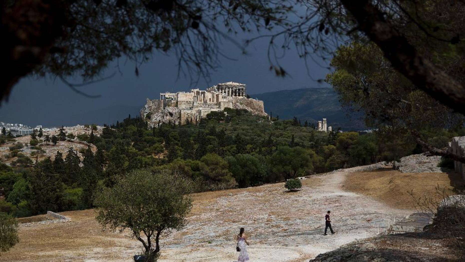 Tourist walk on Pnyx hill in front the ancient Acropolis hill, with the ruins of the fifth century BC Parthenon temple in Athens on Tuesday, June 7, 2016. Beginning as early as 507 BC, the Athenians gathered on the Pnyx to host their popular assemblies, thus making the hill one of the earliest and most important sites in the creation of democracy.(AP Photo/Petros Giannakouris)