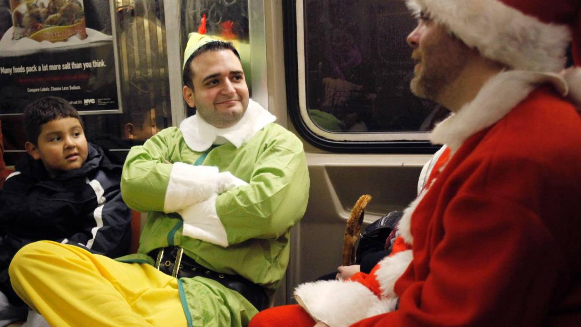 FILE - In this Dec. 11, 2010, file photo, John Paul, center, dressed as an Elf and Michael Smallwood, in a Santa Claus outfit, ride the E train in New York. Paul and Smallwood were participants in SantaCon, an annual holiday pub crawl during which participants dress up as Santa Claus or wear Christmas-themed clothing. As thousands of Santa-suited merrymakers prepare to hit the city's streets and bars Saturday, Dec. 12, 2015, organizers say they're taking steps to deter naughty behavior. (AP Photo/Mary Altaffer, File)