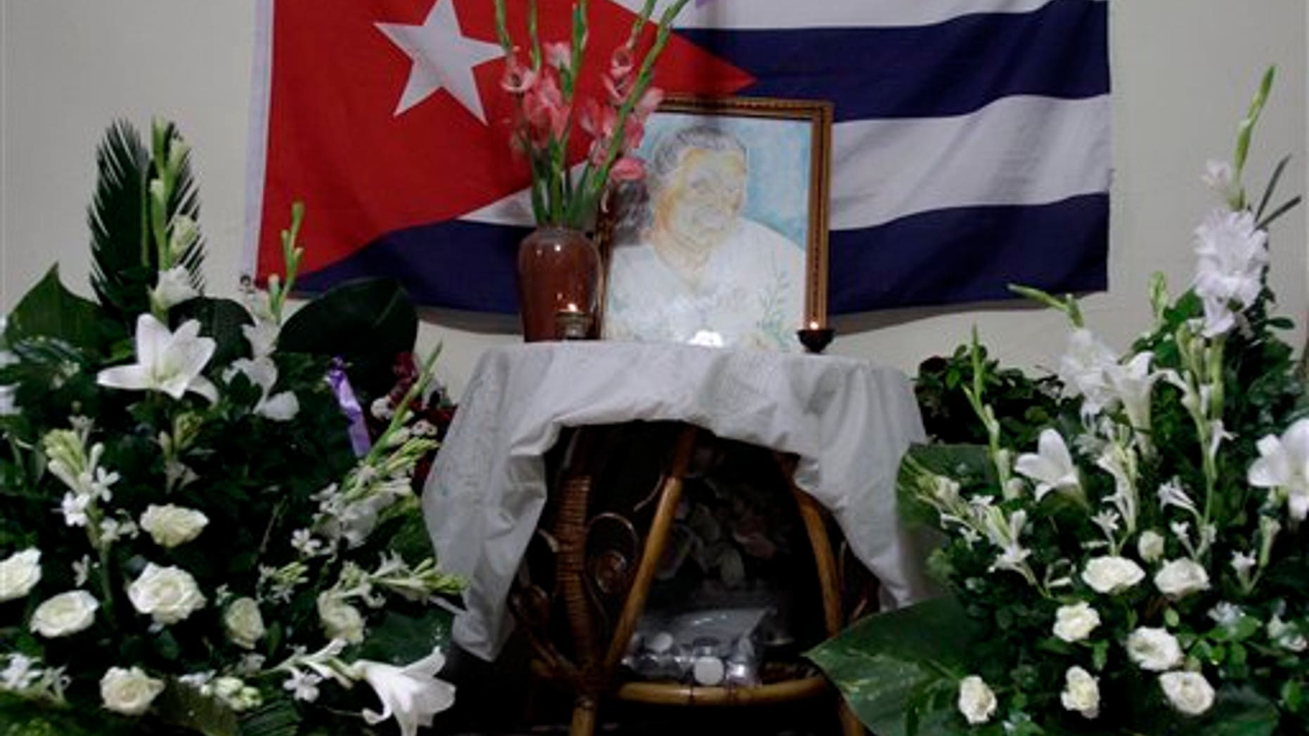 A painting of Laura Pollan, late leader of the dissident group Ladies in White, is flanked by flowers, candles and a Cuban flag during a gathering in her honor at her home in Havana, Cuba, Saturday Oct. 15, 2011.