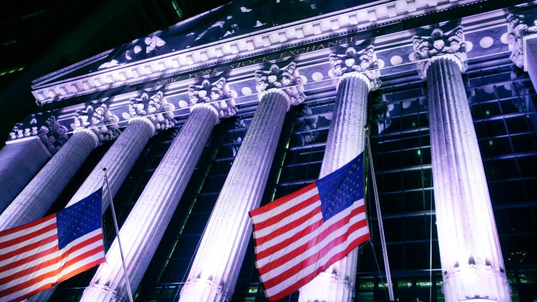 In this Wednesday, Oct. 8, 2014 photo, American flags fly in front of the New York Stock Exchange. U.S. stocks were barely higher in early trading Monday, Dec. 29, 2014, as Wall Street winds down the year in this holiday-shortened week. (AP Photo/Mark Lennihan)