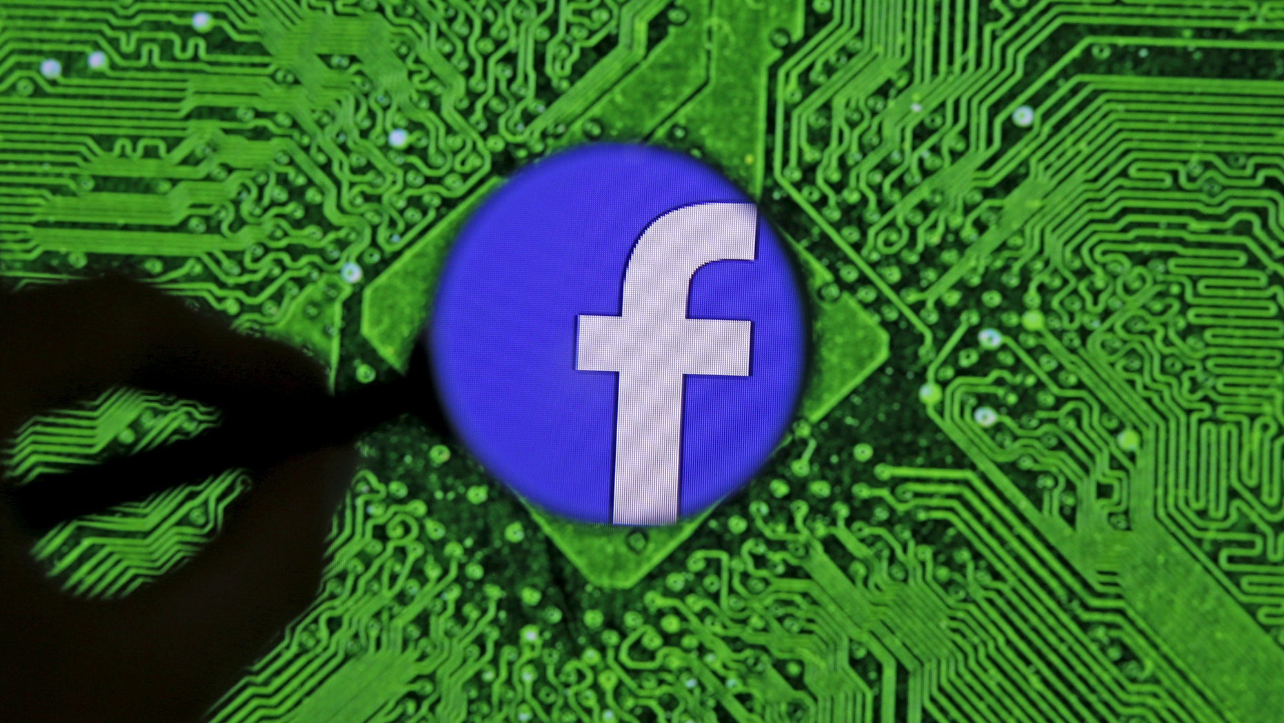 Facebook's logo is seen through a magnifier in front of a displayed PC motherboard, in this illustration taken April 11, 2016. (REUTERS/Dado Ruvic/Illustration)