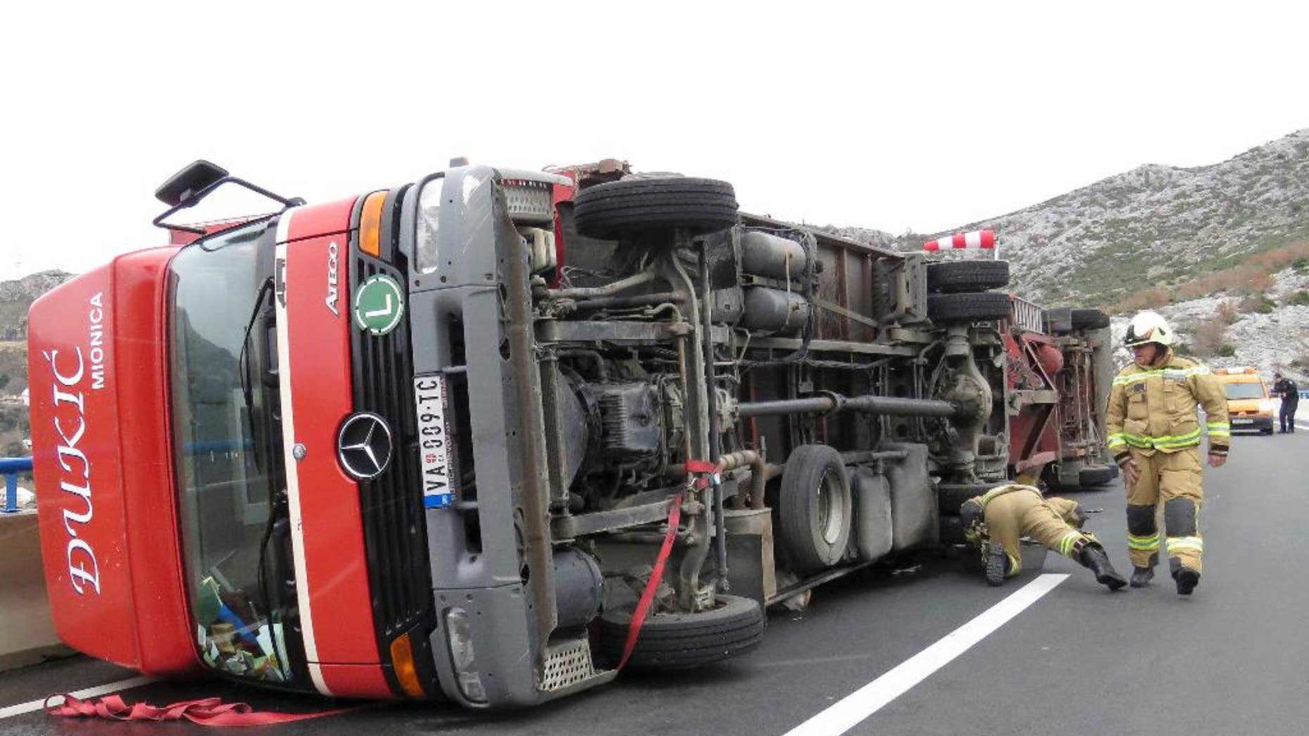 Firemen inspect a truck overturned by heavy winds, near Split, Croatia, Thursday, March 5, 2015. Winds caused traffic disruptions in much of coastal Croatia. (AP Photo/Ivo Cagalj, PIXSELL)