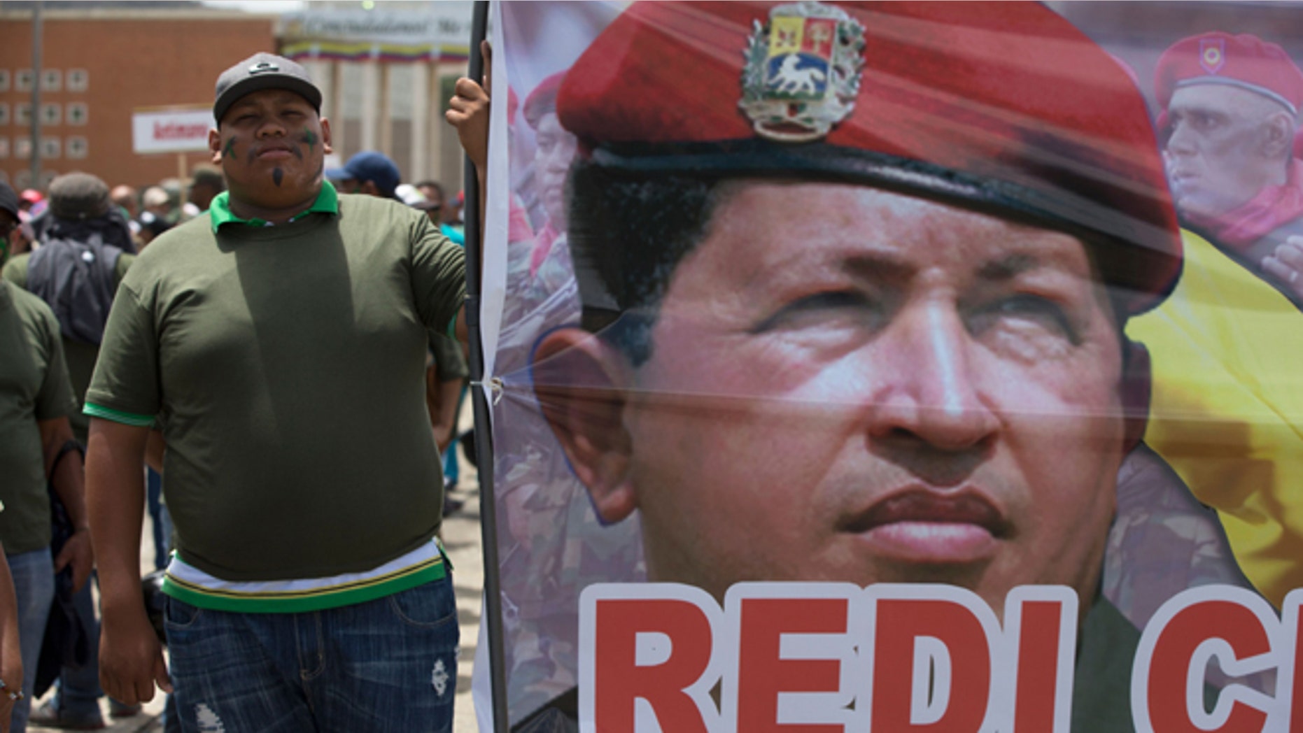 A supporters of Venezuela's President Nicolas Maduro stands next to a picture of Venezuela's late President Hugo Chavez prior a civilian and military exercise at fort Tiuna in Caracas, Venezuela, Saturday, March 14, 2015. President Maduro is expected to oversee military exercises across the country, which are intended to show the South American countryâs strength in the face of U.S. threats. (AP Photo/Fernando Llano)