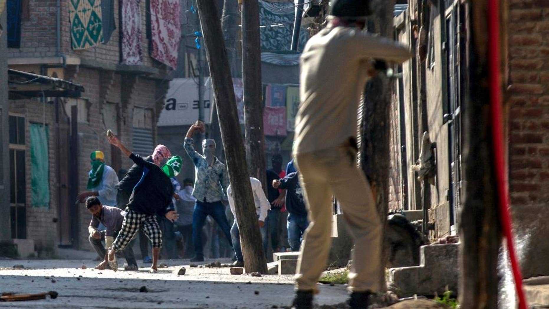 Kashmiri protesters throw stones and bricks at an Indian policeman as he prepares to fire pallet gun during a protest in Srinagar, Indian controlled Kashmir, Friday, Oct. 7, 2016. Authorities imposed a curfew in many parts of the Indian-controlled Kashmir to prevent a protest march to the disputed Himalayan region's office of United Nations Military Observer Group in India and Pakistan (UNMOGIP) called by separatist leaders seeking end of Indian rule. (AP Photo/Dar Yasin)