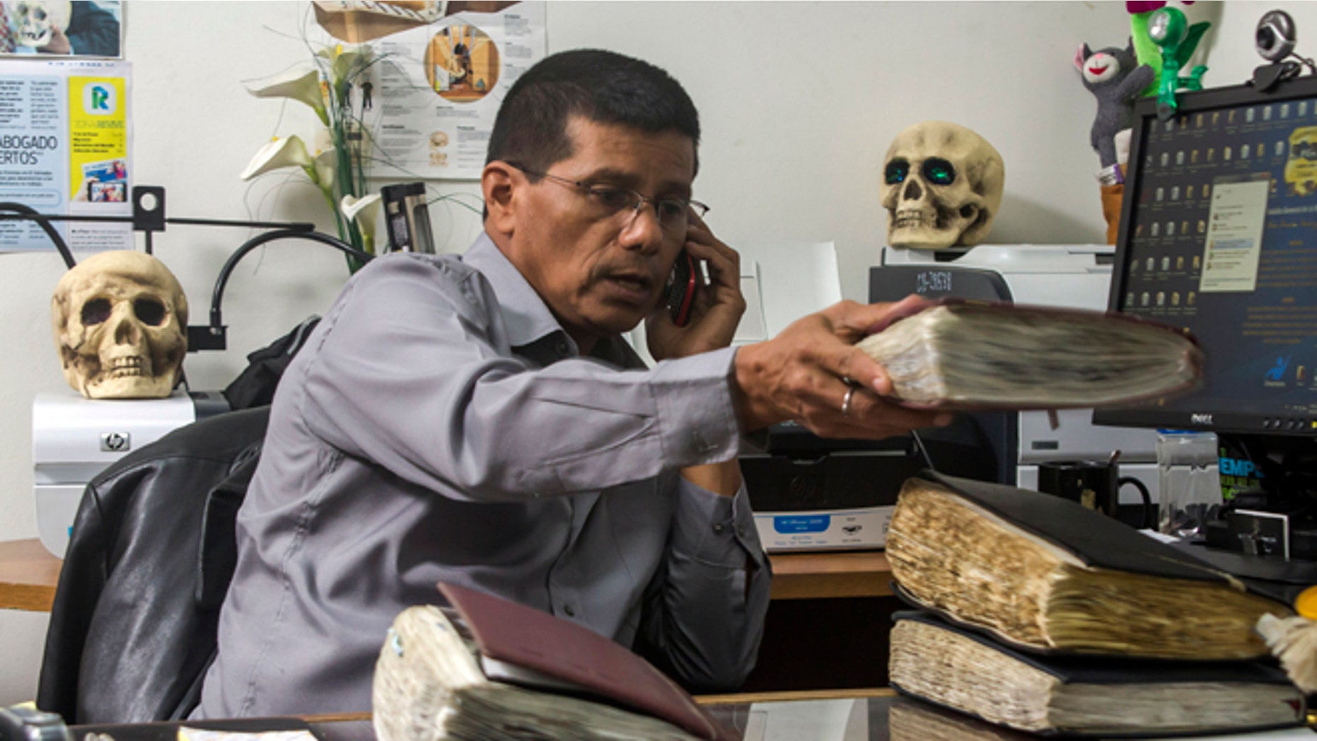 In this Oct. 6, 2014, photo, criminologist Israel Ticas talks on the phone as he stacks his field notebooks, at his office in San Salvador, El Salvador. Ticas got his start making drawings of the dead and models of crime scenes. He studied forensic science on his own and in 2002, convinced the attorney general to give him an office and authority for excavating clandestine cemeteries. (AP Photo/Salvador Melendez)