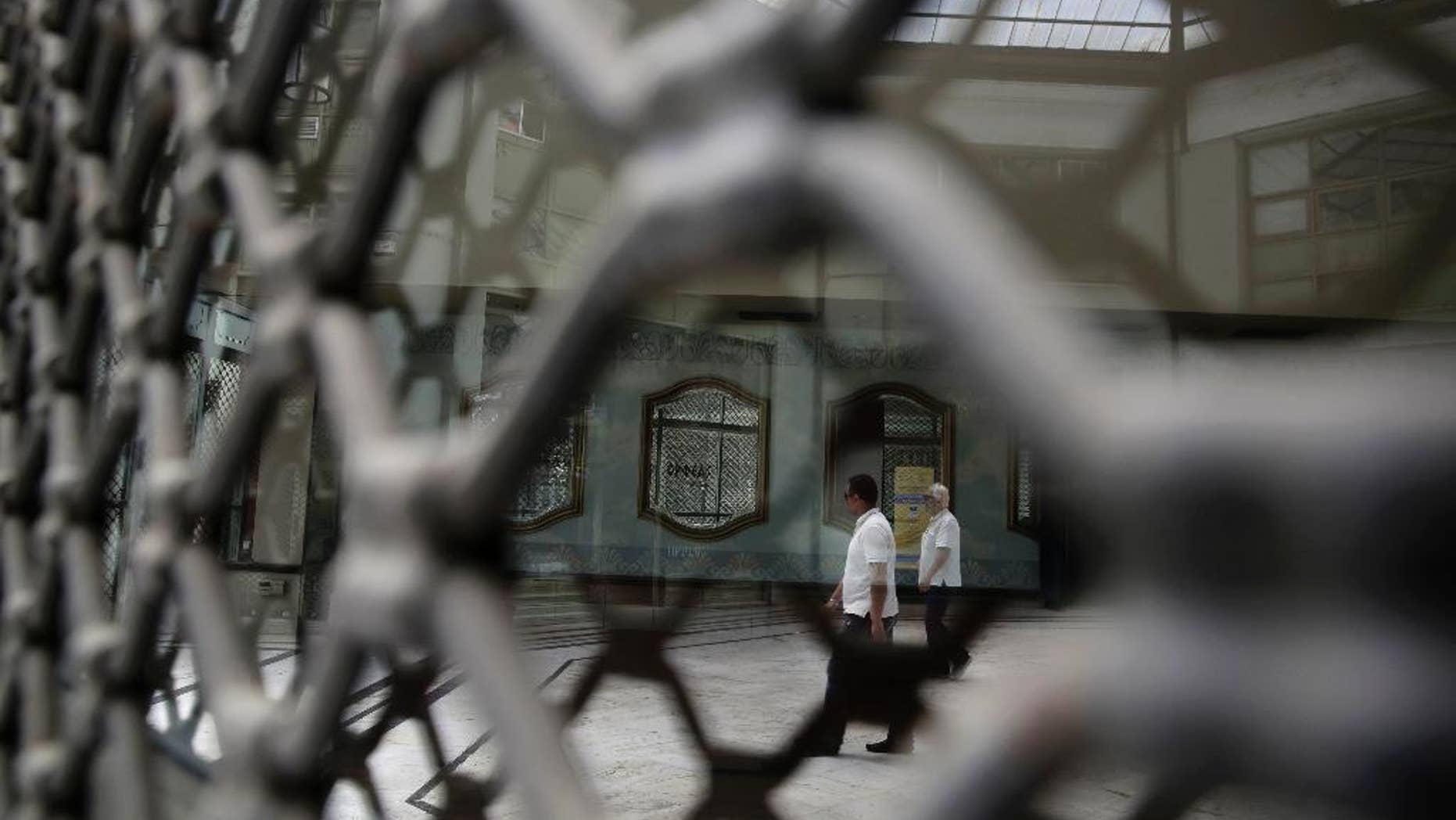 People are reflected on the glass of a shuttered shop as they walk in a shopping arcade, in central Athens, on Monday, May 25, 2015. Greece's radical left-led government has ruled out restricting access to bank accounts and the free movement of capital if there is no breakthrough soon in tortuous negotiations with bailout creditors and the country runs out of money. (AP Photo/Petros Giannakouris)