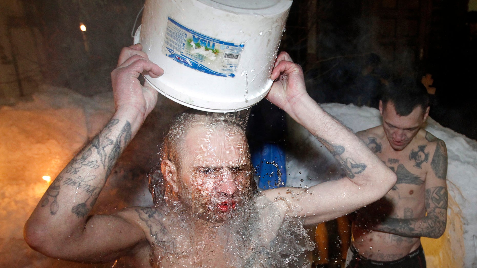 FILE - In this file photo dated Thursday, Jan. 19, 2012, inmates of a prison colony pour cold water over themselves to celebrate Epiphany at St. Peter and Paul Cathedral in the Murmansk region of northern Russia. The contract-style killing of Russian mobster Aslan Usoyan, also known as Grandpa Khasan, on Wednesday Jan16, 2013, drew renewed attention to the extensive and elaborate culture of the country’s underworld figures who call themselves “crowned thieves” and “thieves in law.” Only top criminals are allowed to have tattoos which signal their privileged status within the criminal underworld, and may contain obscure codes, such as MIR (peace) meaning “Only capital punishment will correct me, and the Nazi swastika means rejection of everything Soviet (but does not make its bearer a neo-Nazi). (AP Photo/ Andrey Pronin, FILE)