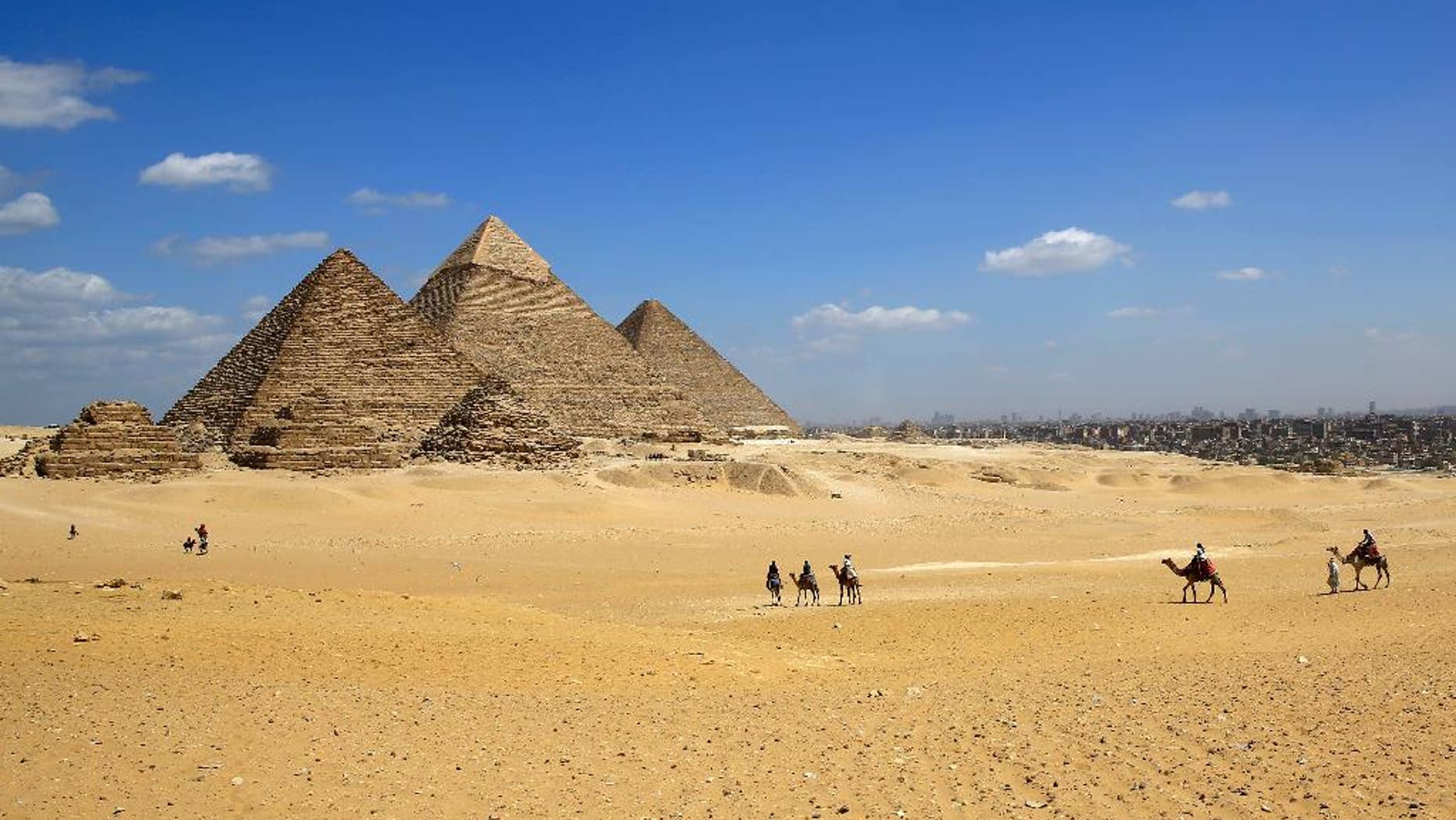 FILE - In this Thursday, April 9, 2015, file photo, tourists ride camels at the historical site of the Giza Pyramids in Giza, near Cairo, Egypt. Gunmen on a speeding motorcycle opened fire outside the plateau of the famed Giza Pyramids on the outskirts of Cairo early Wednesday, killing two policemen, in a rare attack near the country’s tourist attractions, Egypt’s state news agency and security officials said. (AP Photo/Hassan Ammar)