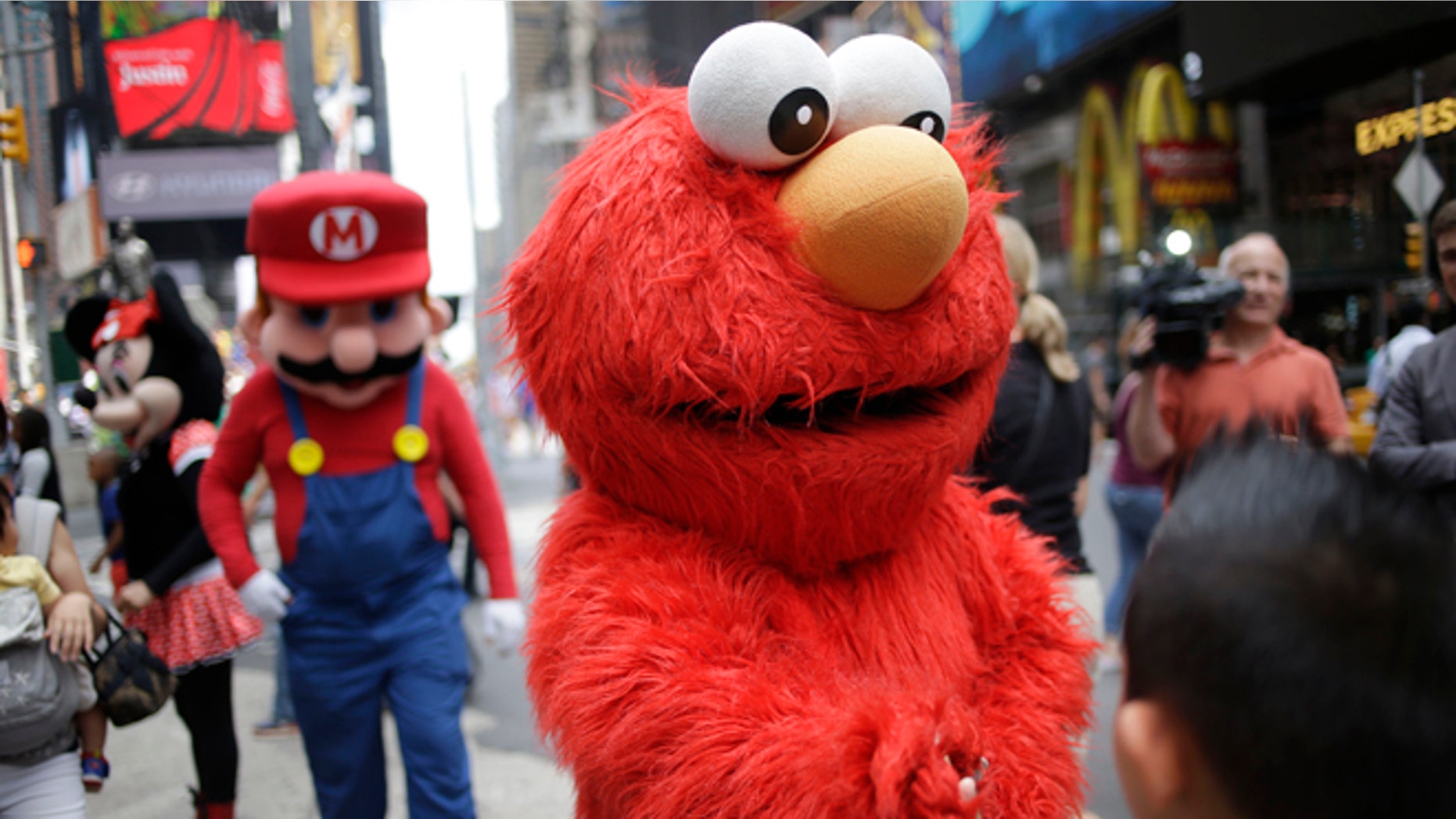 A person dressed as Elmo shakes hands with a pedestrian in Times Square on Monday, July 28, 2014 in New York. New York City Mayor Bill de Blasio said Monday that he believes the people wearing character costumes in Times Square should be licensed and regulated. Dozens of people dressed as kids favorites like Elmo, Cookie Monster and Batman stand near 42nd Street and pose for photos with tourists in exchange for money. De Blasio said the practice has gone too far. A man dressed as Spider-man was arrested Saturday, July 28, 2014, after punching a police officer who told him to stop harassing tourists. The City Council is working on legislation that would require the characters to get a city-approved license. (AP Photo/Seth Wenig)