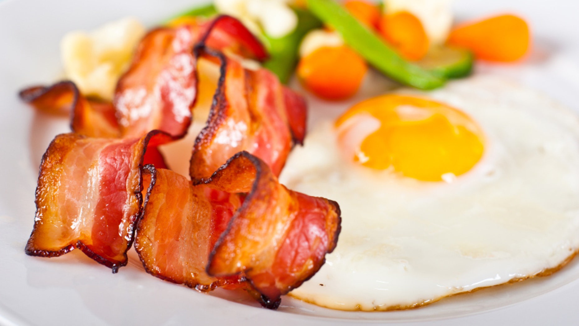 Close-up of fried egg with bacon and vegetables.
