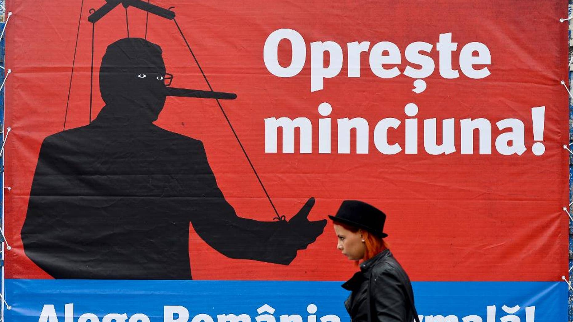 A woman walks backdropped by a campaign poster of Klaus Iohannis leader of Romania's centre-right Liberals and mayor of the Transylvanian city of Sibiu, showing a mock representation of Prime Minister and candidate of the ruling Social Democracy Party (PSD) together with the texts "Stop the lying!" and "Choose the normal Romania!", in Bucharest, Romania, Monday, Nov. 10, 2014. Top party lieutenants in Ponta’s Social Democratic Party, regular party members and other supporters have been convicted or are being probed for corruption, but Ponta appears unscathed. An election runoff will be held on Nov. 16., to elect a new leader as President Traian Basescu steps down after 10 years in office. (AP Photo/Octav Ganea, Mediafax) ROMANIA OUT