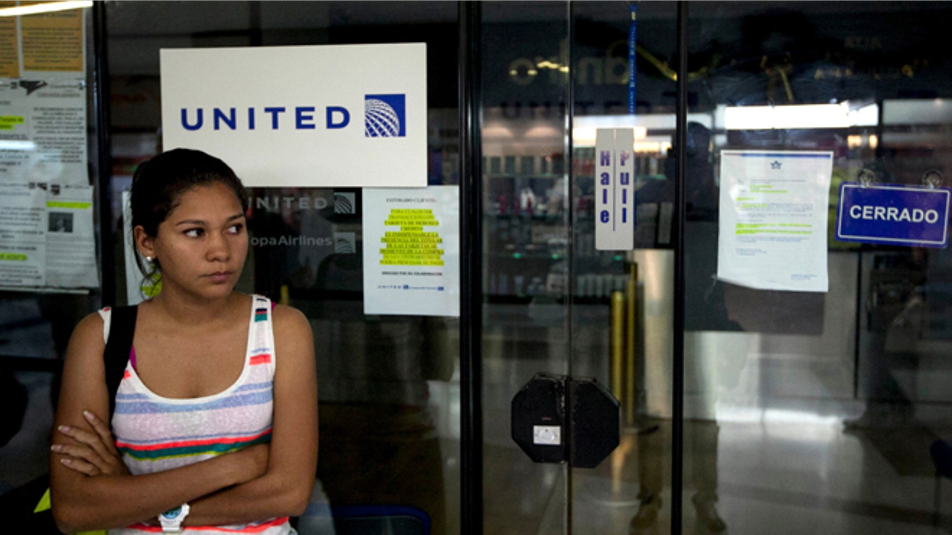 FILE- In this Jan. 24, 2014 file photo, a woman stands outside a closed United Airlines office in Caracas, Venezuela. Alitalia and Panamas Copa Airlines this May 2014, became the latest carriers to cut flights to Caracas over the socialist governments refusal to allow them to repatriate proceeds from ticket sales inside Venezuela. Foreign airlines say they have the equivalent of $4 billion trapped in the country when sales are converted at the official exchange rate of 6.3 bolivars per U.S. dollar. (AP Photo/Alejandro Cegarra)