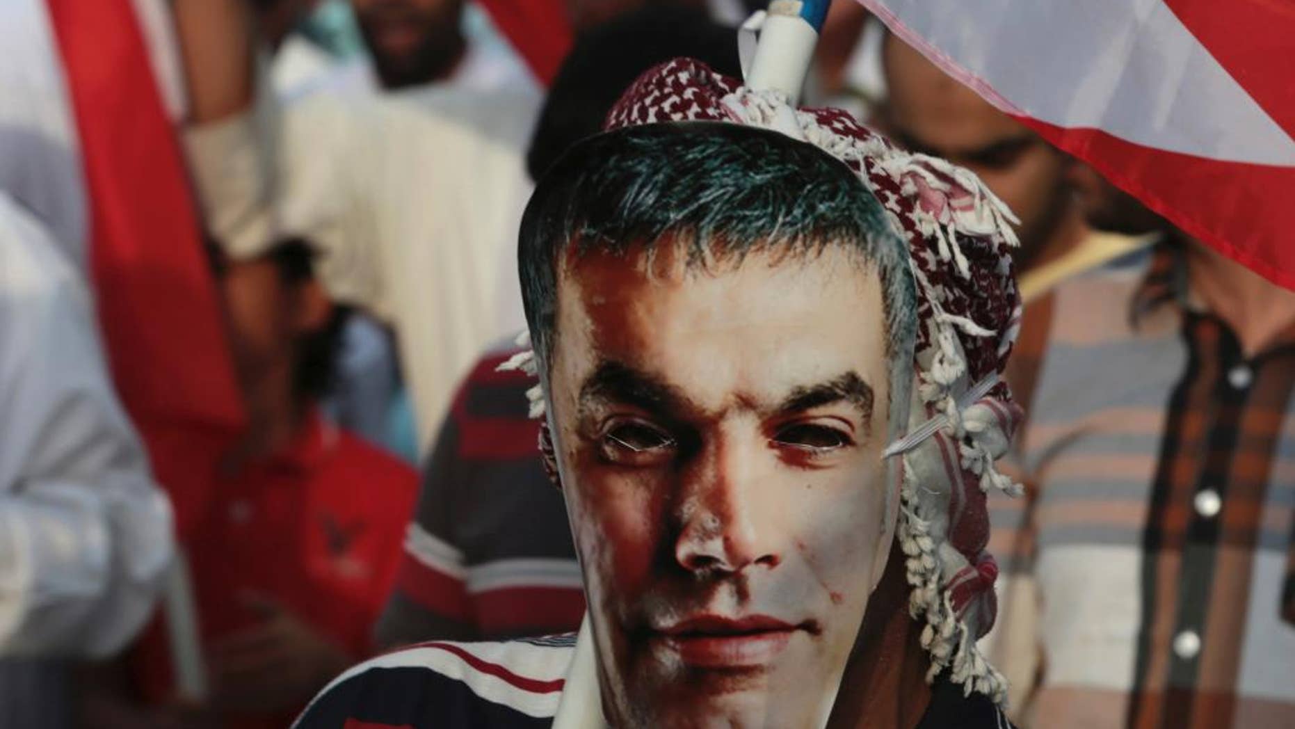 FILE - In this Friday, March 21, 2014 file photo, a Bahraini pro-democracy protester wears a mask with an image of jailed Bahraini human rights activist Nabil Rajab as others wave national flags during a march in Abu Saiba, west of the capital, Manama, Bahrain. The country's official news agency reported Monday, July 13, 2015, that King Hamad bin Isa Al Khalifa has pardoned Rajab, an outspoken human rights activist on health grounds after three months in prison. (AP Photo/Hasan Jamali, File)