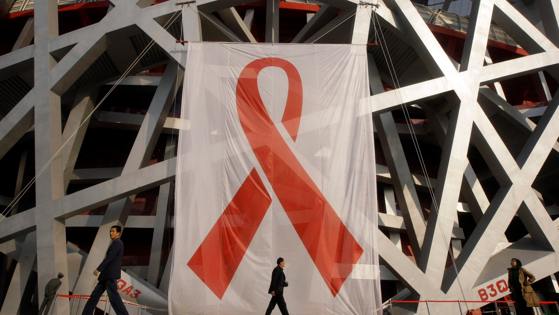 People walk past a giant red ribbon set up on the facade of the "Bird's Nest" during a World AIDS Day event in Beijing November 30, 2008. There are about 700,000 cases of HIV/AIDS in China, according to official statistics. REUTERS/Jason Lee (CHINA) - RTR2242U