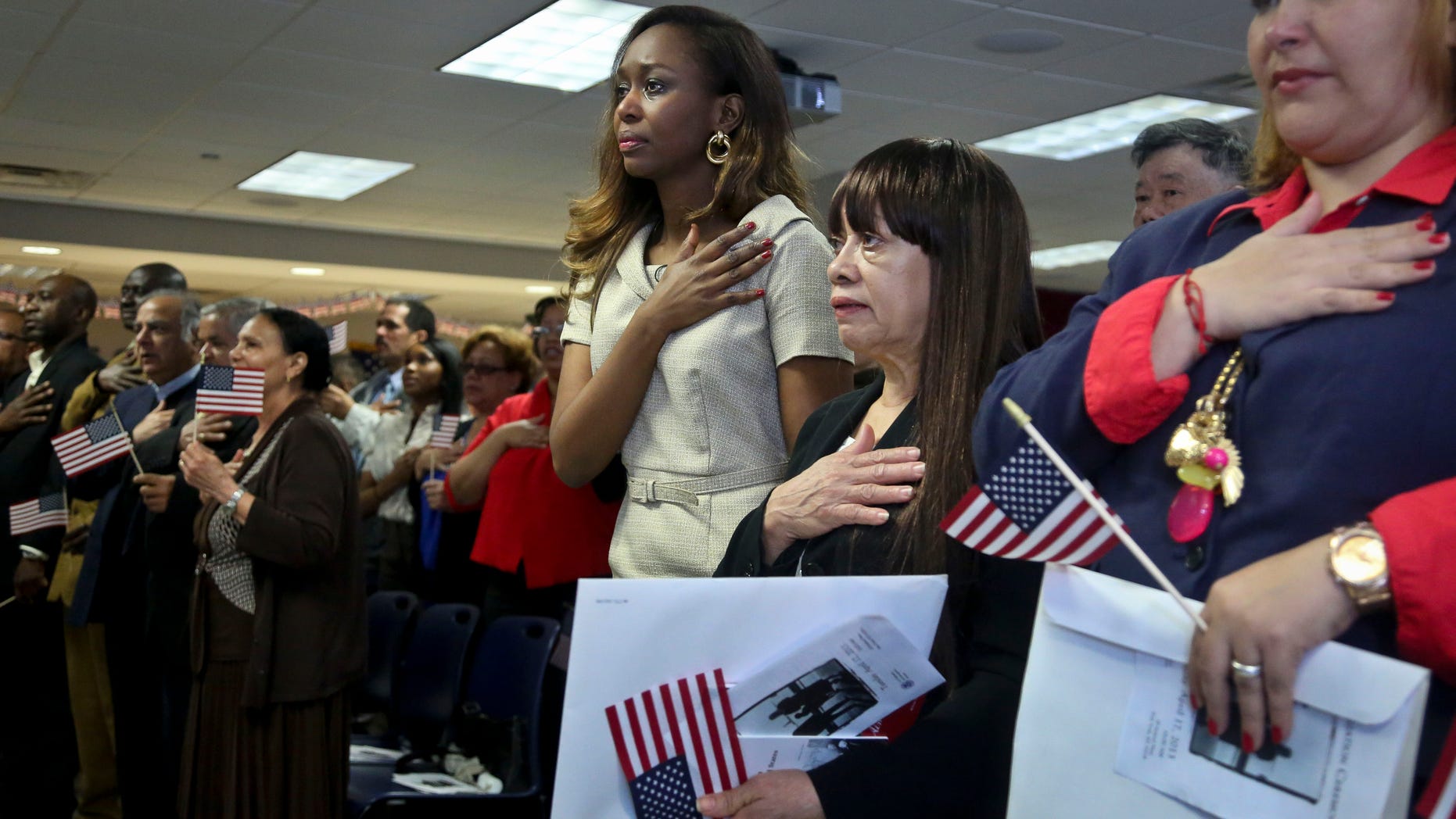Immaculee Ilibagiza, fourth from right, center, join new immigrants in the pledge allegiance, during the U.S. Citizenship and Immigration Services (USCIS) naturalization ceremony on Wednesday, April 17, 2013 in New York. Ilibagiza, author of the best seller “Left to Tell, Discovering God Amidst the Rwandan Holocaust,” addressed fellow immigrants with her story of hiding in a 3-by-4 foot bathroom with seven other women and girls before fleeing the 1994 Rwandan genocide, which claimed more than 500,000 lives. (AP Photo/Bebeto Matthews)