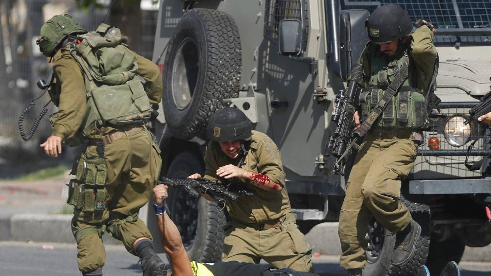 FILE - In this Friday, Oct. 16, 2015, file photo, an Israeli soldier runs to help another who was just stabbed by a Palestinian, seen on the ground holding a knife, during clashes in Hebron, West Bank. The clashes between Israelis and Palestinians in the Holy Land are not just physical; the two sides cannot agree on what they see, how they got here, who is to blame or where they should go. (AP Photo/Nasser Shiyoukhi, File)