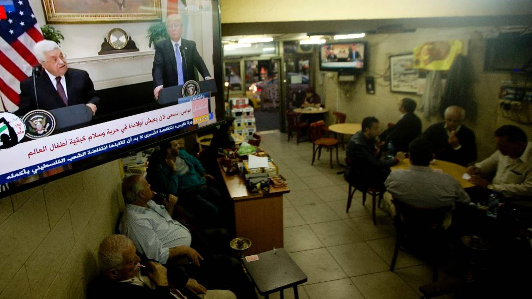Palestinians play cards at a coffee shop as a television broadcasts a statement in Washington between President Donald Trump with Palestinian President Mahmoud Abbas, in the West Bank city of Ramallah, Wednesday, May 3, 2017. Trump said Wednesday that the White House is starting a process between the Israelis and Palestinians that "hopefully will lead to peace." Abbas said that he's hopeful for bringing about peace with Israel "based on the vision of two states," with the borders of 1967. Israel has rejected the 1967 lines as a possible border, saying it would impose security risks. (AP Photo/Majdi Mohammed)