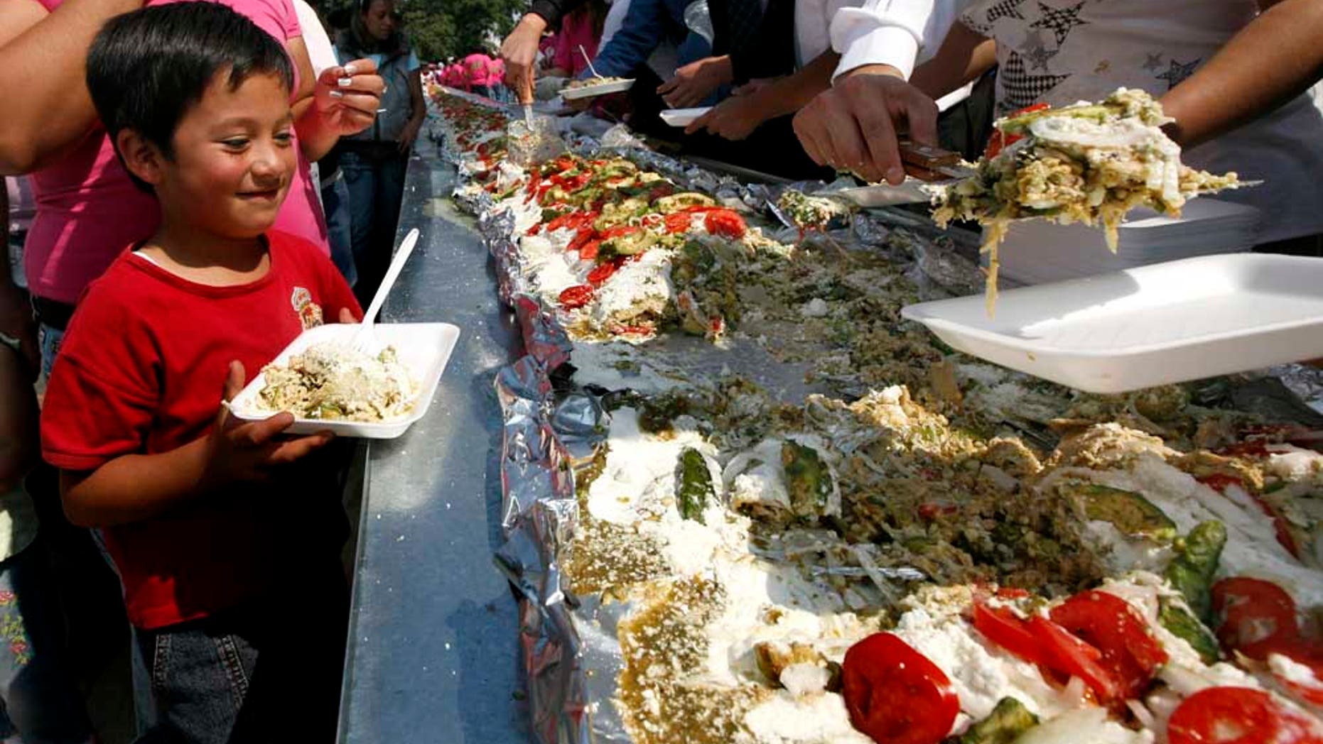 A boy waits to be served a portion of the world's largest 'Enchilada', a traditional Mexican food, during the National Enchilada Fair at the neighborhood of Iztapalapa in Mexico City, Sunday, Oct. 17, 2010. The enchilada, measuring 70 meters long and 1,416 kgs, entered the famous Guinness Record book Sunday. (AP Photo/Marco Ugarte)