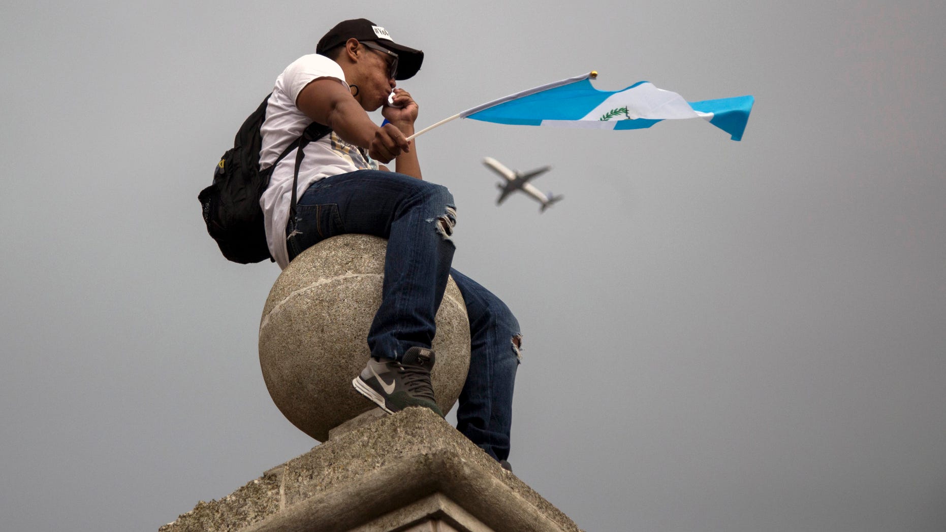 En esta imagen, tomada el 27 de agosto de 2015, un manifestante ondea una bandera de Guatemala sentado en lo alto de una columna en la catedral Metropolitana durante una huelga nacional para exigir la renuncia del presidente del país, Otto Pérez Molina, en la ciudad de Guatemala. La presión sobre el mandatario va en aumento, con negocios y oficinas gubernamentales cerradas y multitudinarias protestas, mientras el fiscal general del Estado le instó a dimitir "para evitar una ingobernabilidad que podría desestabilizar la nación". (Foto AP/Luis Soto)