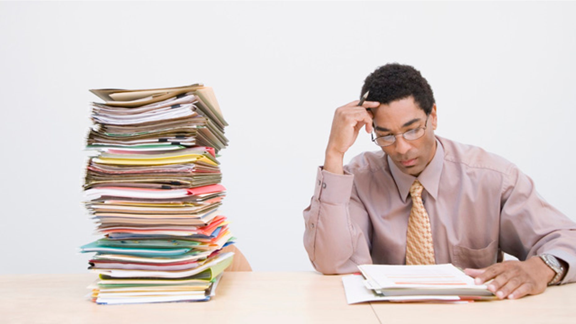 Businessman sitting next to stack of documents on desk, clocks on wall