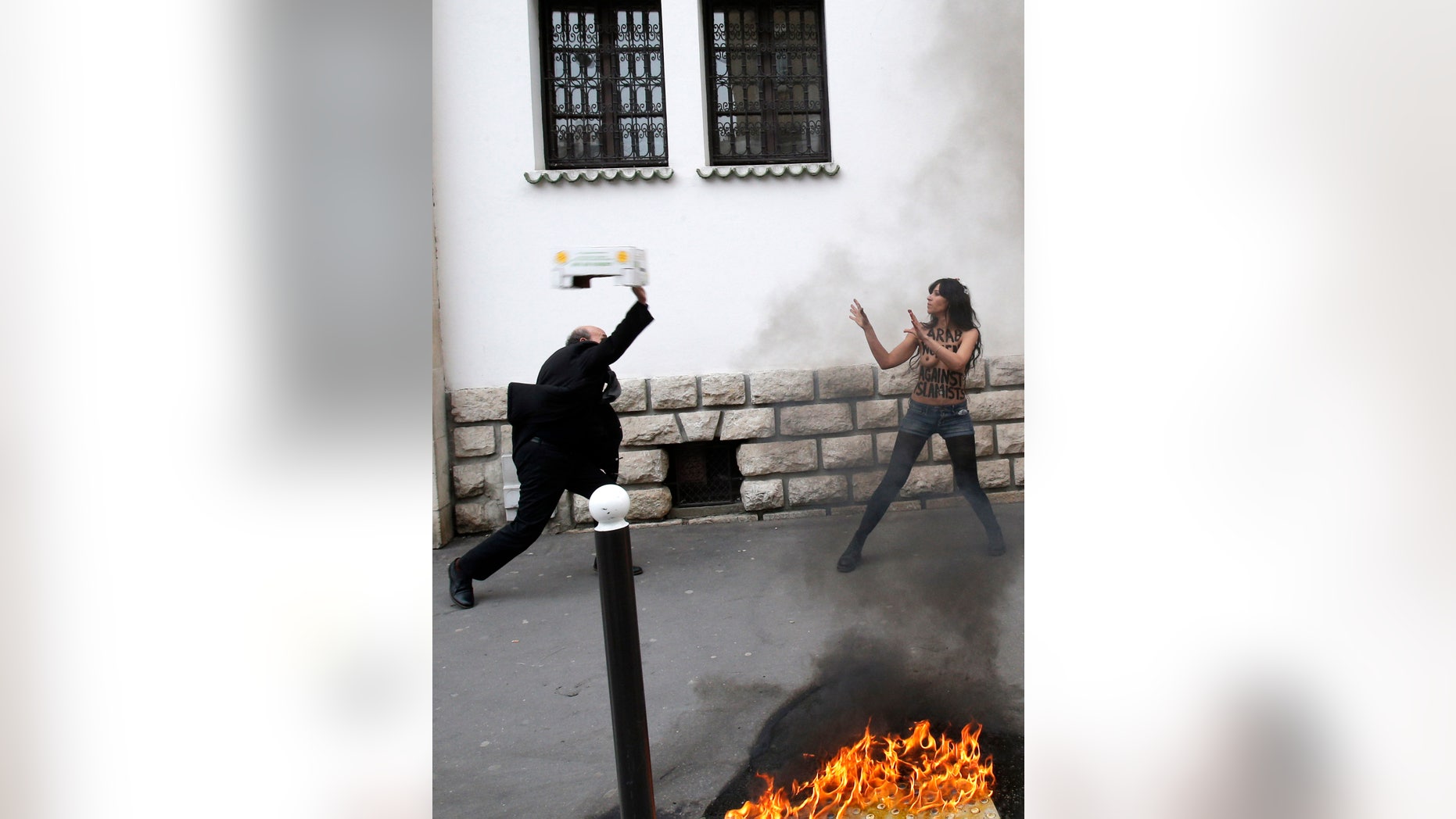 EDS NOTE: NUDITY - A man throws a box toward a FEMEN activist during a protest in front of the Grand Mosque in Paris, Wednesday, April 3, 2013. The radical feminists, calling for more sexual freedom for Arab women, were protesting in support of a young Tunisian woman who received online death threats from ultraconservative Muslims after posting topless photos of herself online. (AP Photo/Christophe Ena)