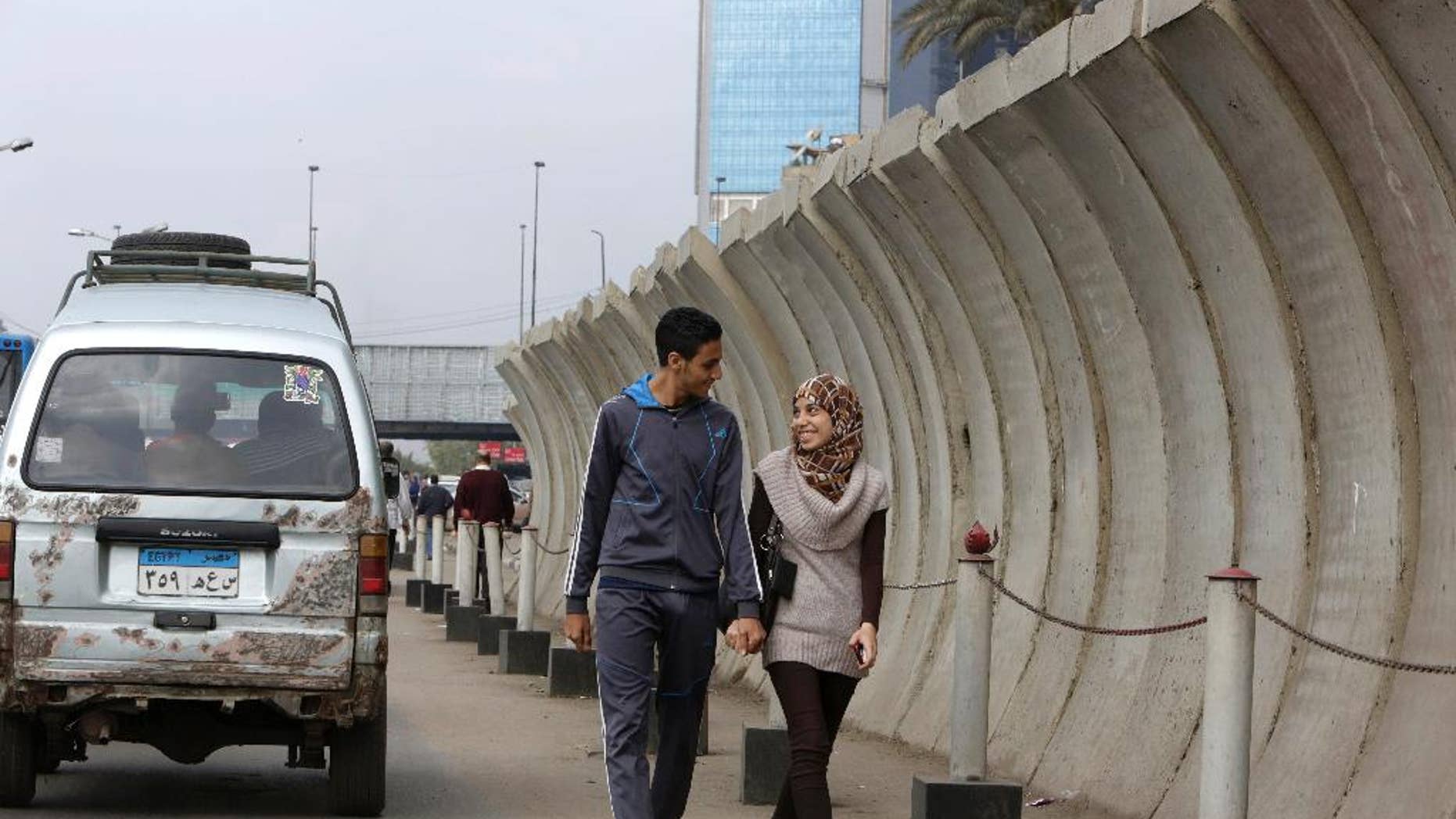 Egyptian couple walks past a concrete barrier surrounding the foreign ministry in Cairo, Egypt, Thursday, Nov. 27, 2014. Egypt's interior minister warned Tuesday that his forces will use deadly force to counter any assault against public facilities in a message coming just ahead of a planned protest by Islamists. (AP Photo/Amr Nabil)