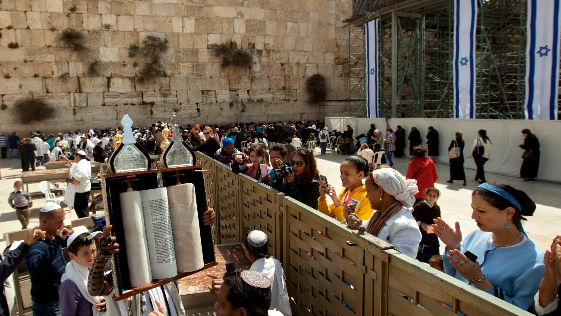 A man holds up a Torah scroll as women stand across a fence at the Western Wall, the holiest site where Jews can pray in Jerusalem's old city, Wednesday, April 10, 2013. The rabbi of Judaism's holiest prayer site has backed a proposal to establish a prayer section for mixed-gender worship, a groundbreaking motion that could end a decades-old fight against Orthodox monopoly of the area. (AP Photo/Sebastian Scheiner)