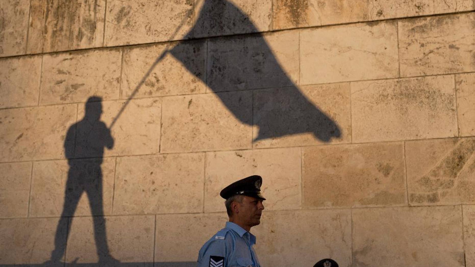 The shadow of a demonstrator waving a flag is cast on a wall as a Greek police officer secures the Greek Parliament during a protest in central Athens, Wednesday, June 15, 2016. Several thousand anti-government protesters gathered in central Athens Wednesday to demand the resignation Prime Minister Alexis Tsipras, accusing his government of breaking promises to end austerity and sinking the country deeper into financial distress.(AP Photo/Petros Giannakouris)