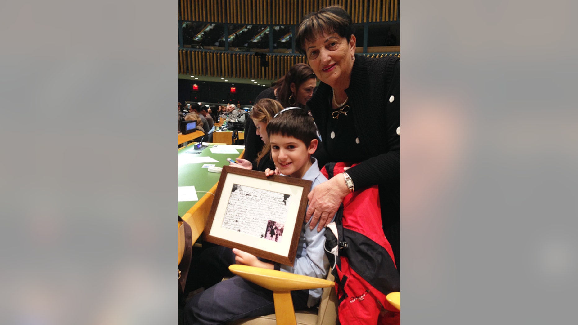 Amnon Schariawith his grandmother, Rita Scharia at the United Nations annual Holocaust Commemoration Ceremony in New York. Rita is a Holocaust survivor who traveled from Israel to be at the commemoration with her grandson and his family. Amnon is holding the last postcard she saved from her father who perished on the way to Auschwitz.