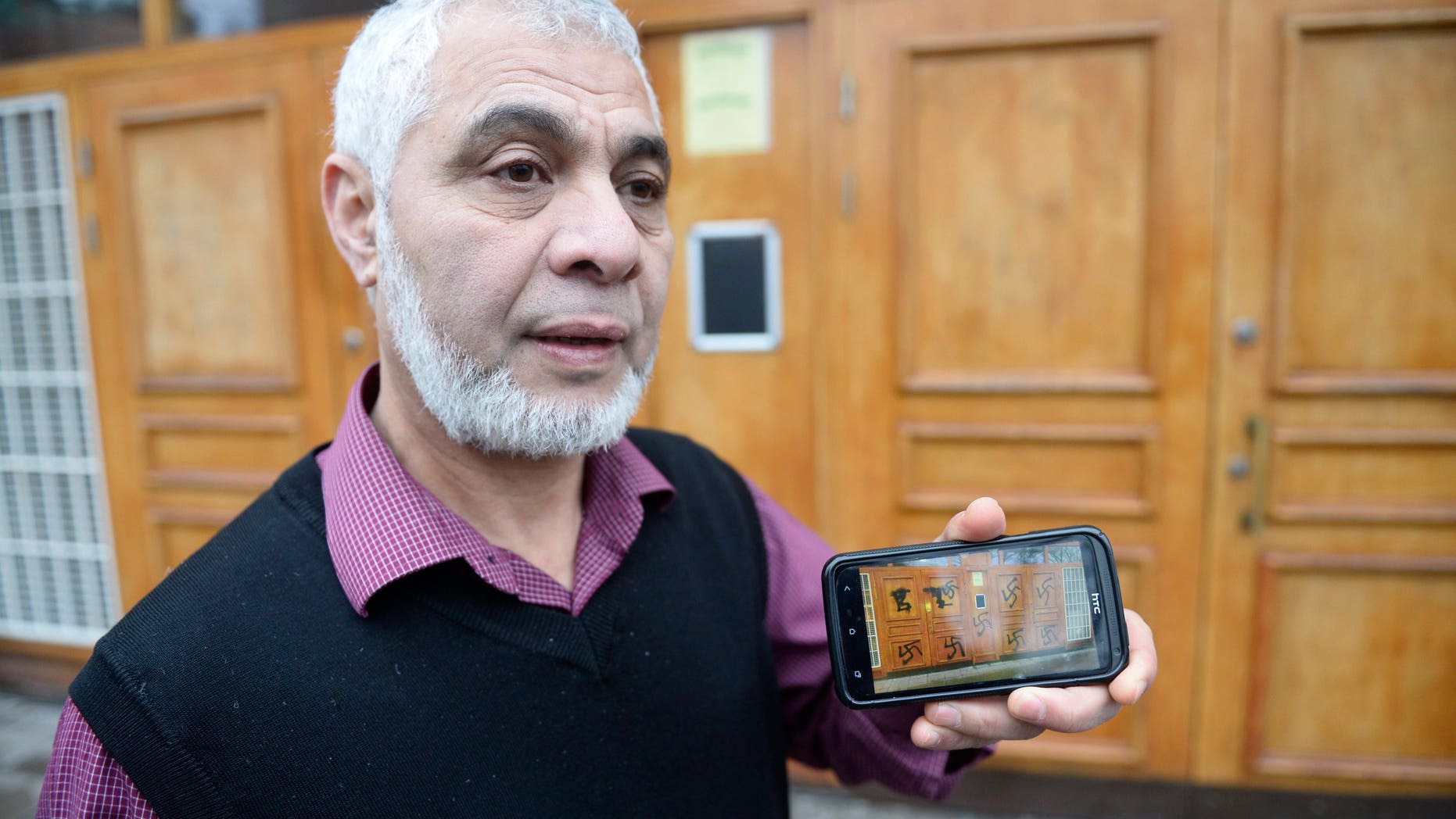 Imam Mamut Kalfi shows on his mobile phone the pictures he has taken of the vandalism that took place on the doors to the central Stockholm mosque Thursday, Jan. 2, 2014. Swedish police have opened a hate crime investigation after the swastikas were spray-painted on the entrance of the mosque in Stockholm. Omar Mustafa, the head of Sweden’s Islamic federation, said employees discovered the vandalism as they arrived to open the mosque Thursday morning. Mustafa said the mosque is targeted by hate mail or vandalism about twice a month, but this is the first time someone’s defaced the entrance with swastikas since the mosque was built in 2000. (AP Photo/TT, Leif R Jansson) SWEDEN OUT