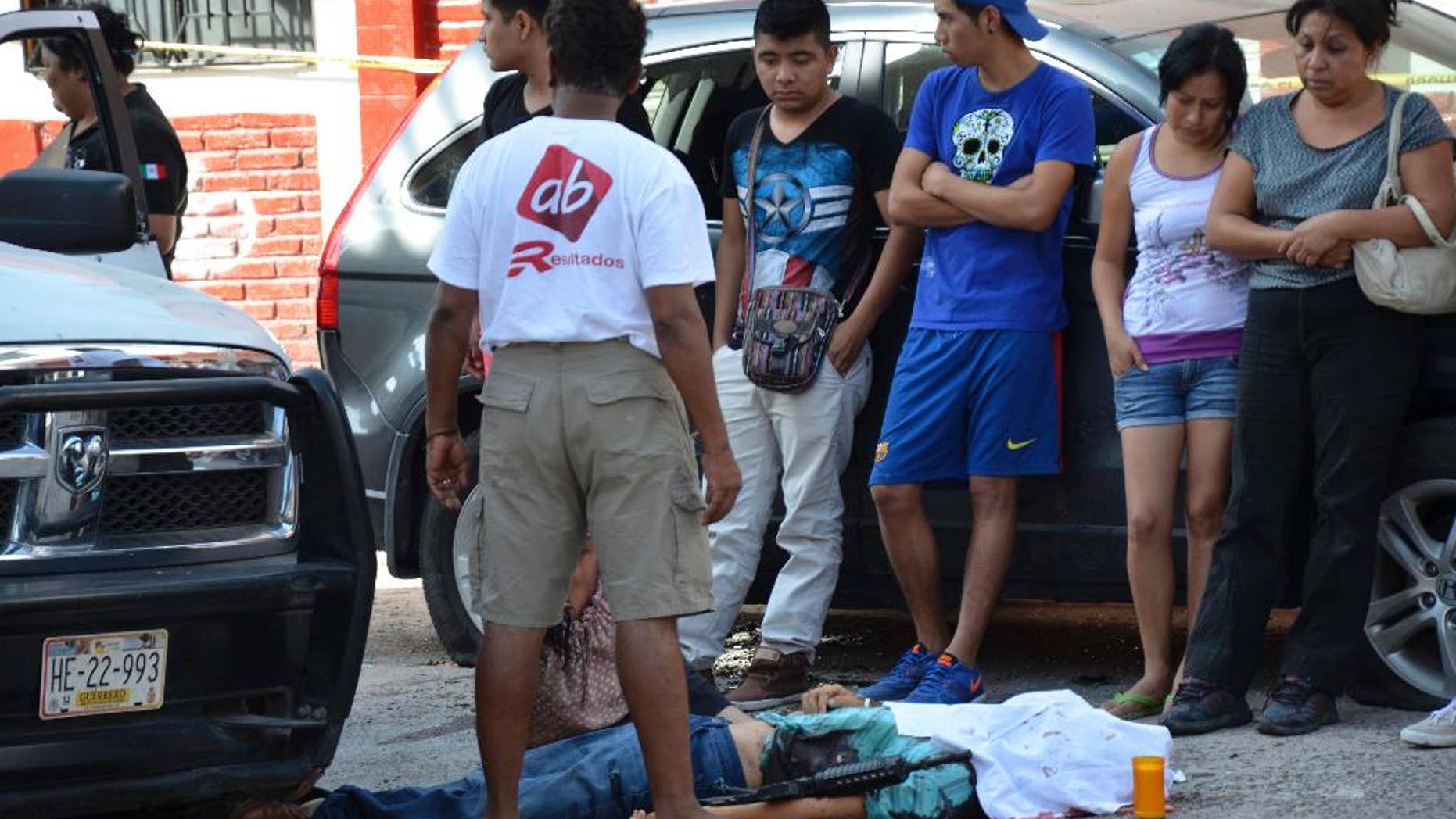 People stand next to the body of police commander David Urquizo Molina after he was gunned down in the city of Chilpancingo, Guerrero State, Mexico, Thursday, July 30, 2015. About two hours later, authorities pursuing the suspected gunmen killed three. Three others were wounded and seven were arrested. Guerrero has been racked with violence as competing drug cartels clash frequently with police and soldiers. (AP Photo/Alejandrino Gonzalez)