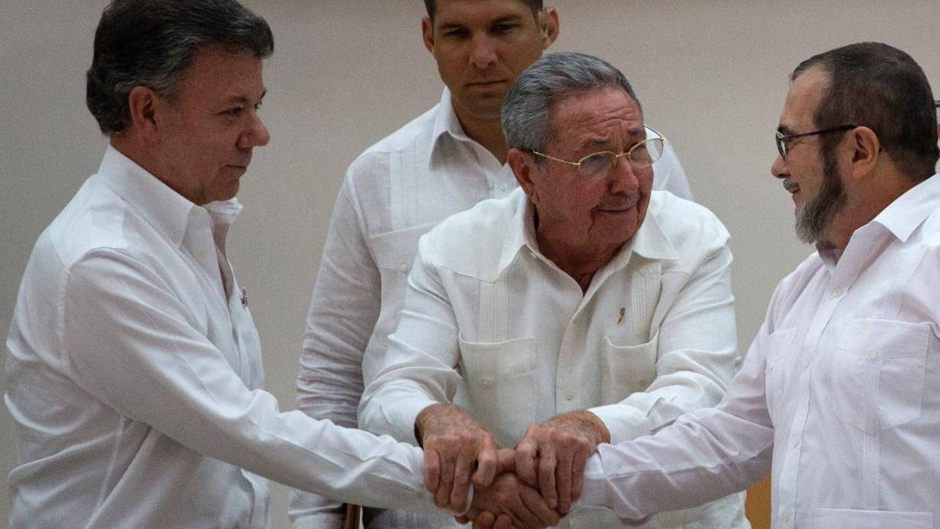 In this Wednesday, Sept. 23, 2015 photo, Cuba's President Raul Castro, center, encourages Colombian President Juan Manuel Santos, left, and Commander the Revolutionary Armed Forces of Colombia or FARC, Timoleon Jimenez to shake hands, in Havana, Cuba. In a joint statement, Santos and the FARC said they have overcome the last significant obstacle to a peace deal by settling on a formula to compensate victims and punish belligerents for human rights abuses. (AP Photo/Desmond Boylan)