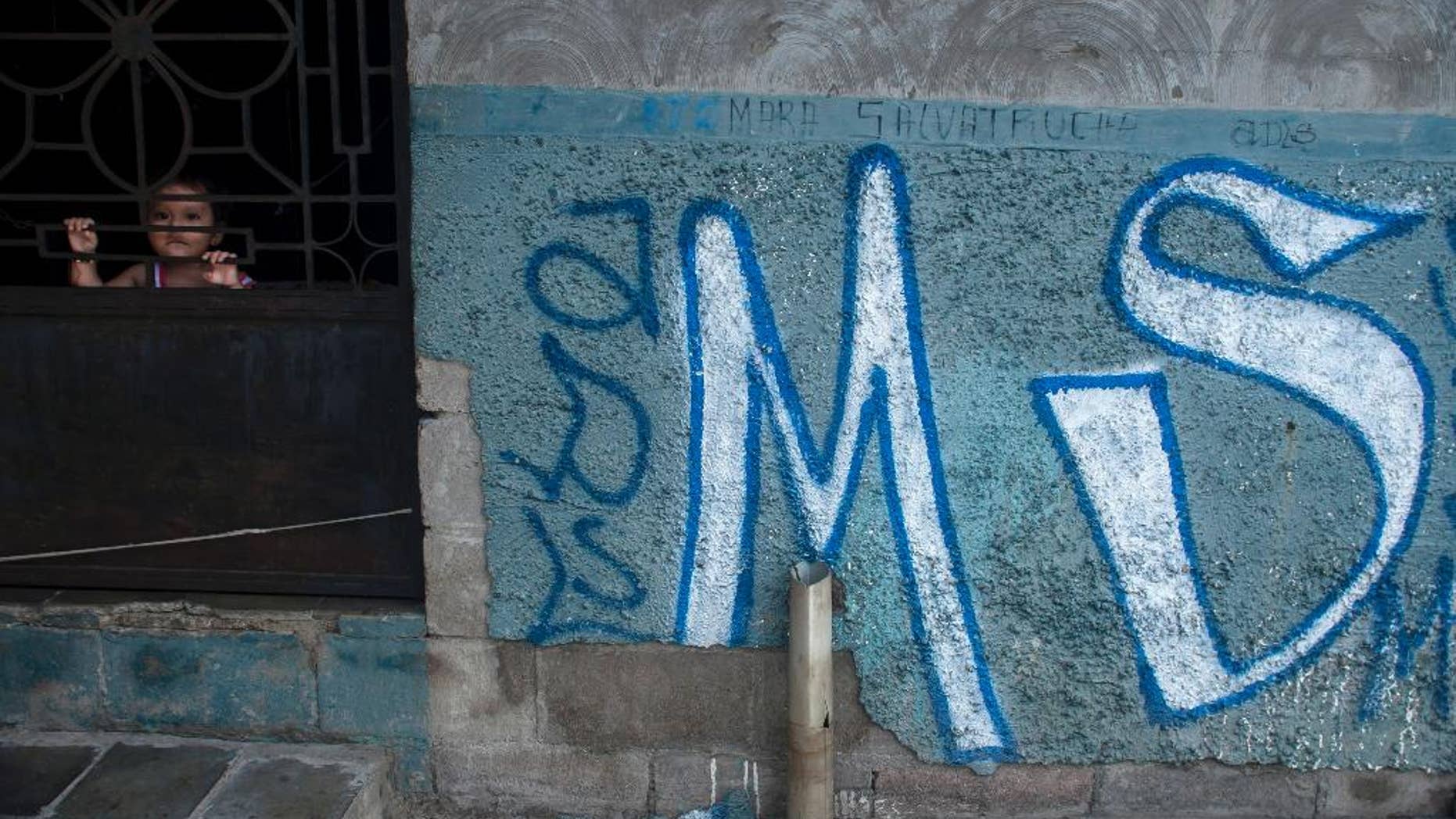 FILE - In this June 21, 2016 file photo, a child peers from behind the door of her home, covered with Mara Salvatrucha gang graffiti, in Soyapango, El Salvador. Attorneys general in Central America are expressing concern on Thursday, April 20, 2017 over comments from their U.S. counterpart suggesting increased deportations of gang members by the United States. (AP Photo/Salvador Melendez, File)
