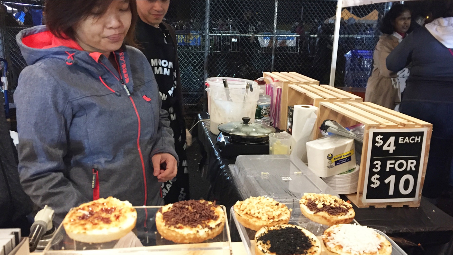 Vendors at the Queens Night Market in New York City's Corona, Queens, neighborhood, selling Indonesian coconut cake snacks with various toppings.