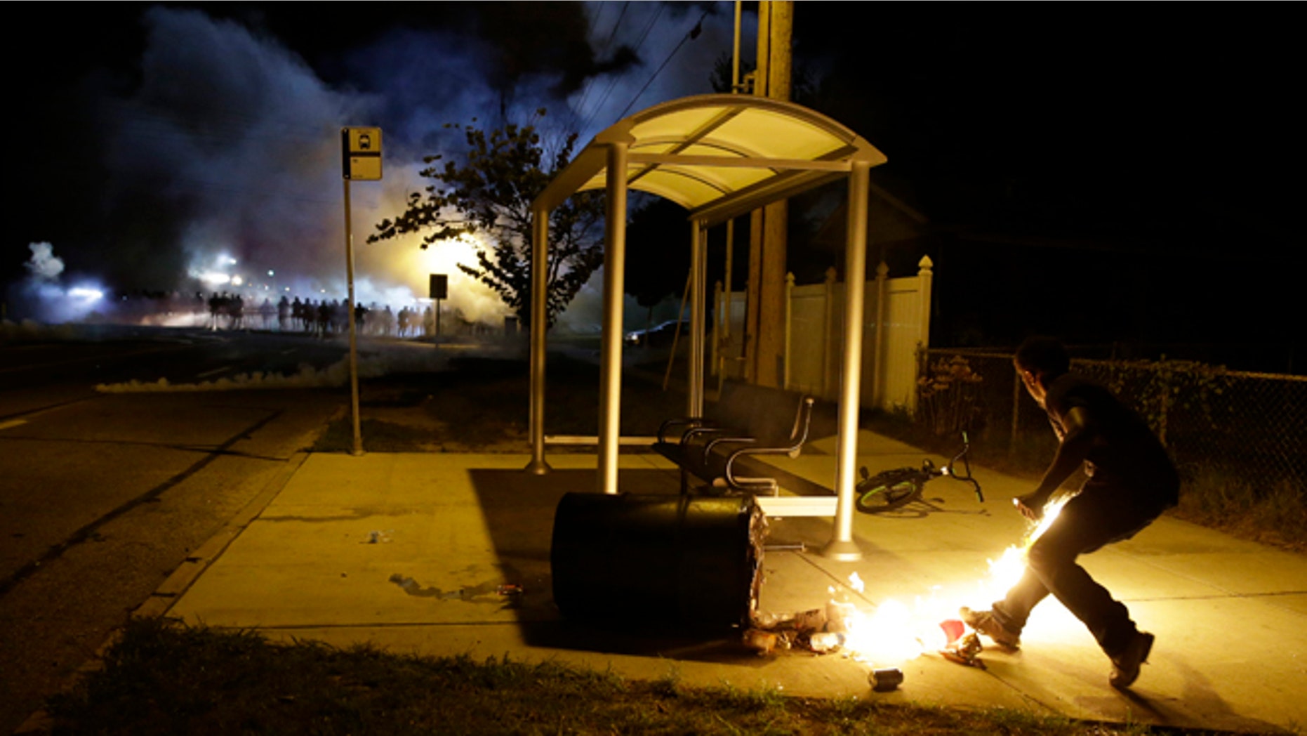 Aug. 13, 2014: A man picks up a flaming bottle and prepares to throw it as a line of police advance in the distance in Ferguson, Mo. (AP/Jeff Roberson)