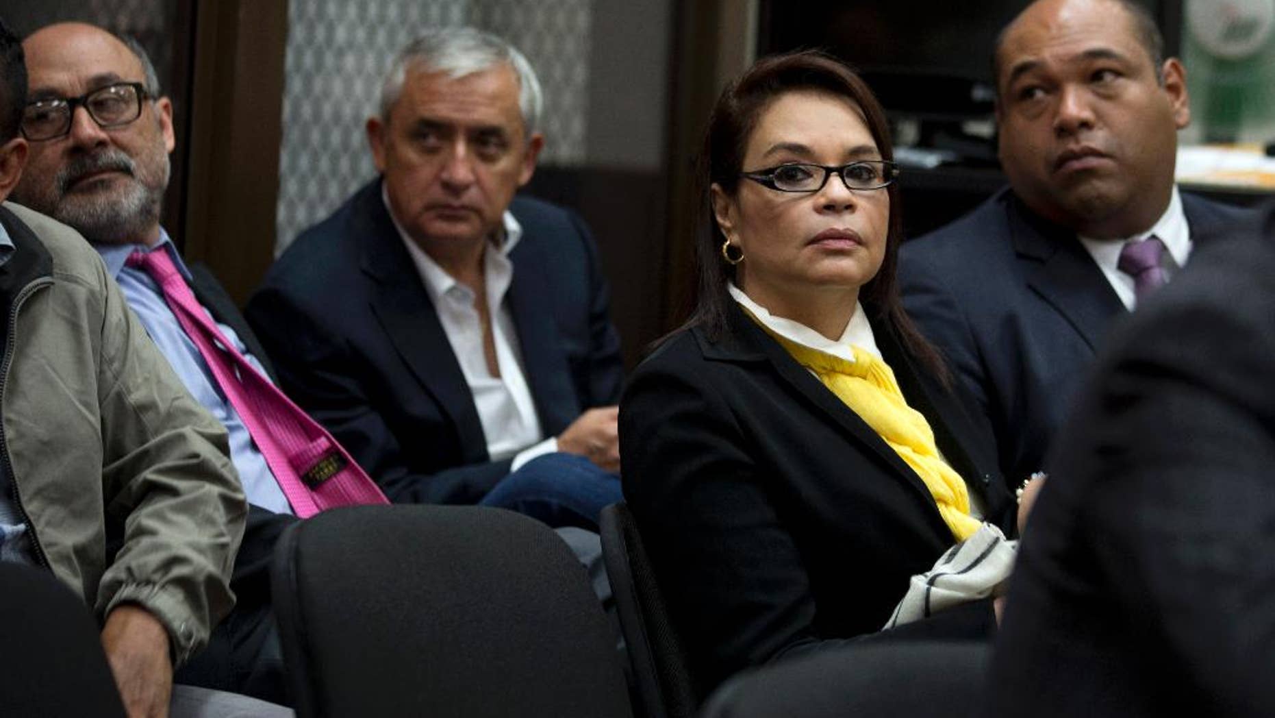 FILE - In this April 20, 2016, file photo, Guatemala's former Vice-President Roxana Baldetti, wearing a yellow scarf, and former President Otto Perez Molina, back center, wait for the start of a court hearing in Guatemala City. Perez and Baldetti have been formally charged on Thursday, June 16, 2016, in a sprawling corruption scheme that emptied government coffers and laundered money to be spent on Miami shopping sprees, real estate and luxury vehicles. (AP Photo/Moises Castillo, File)