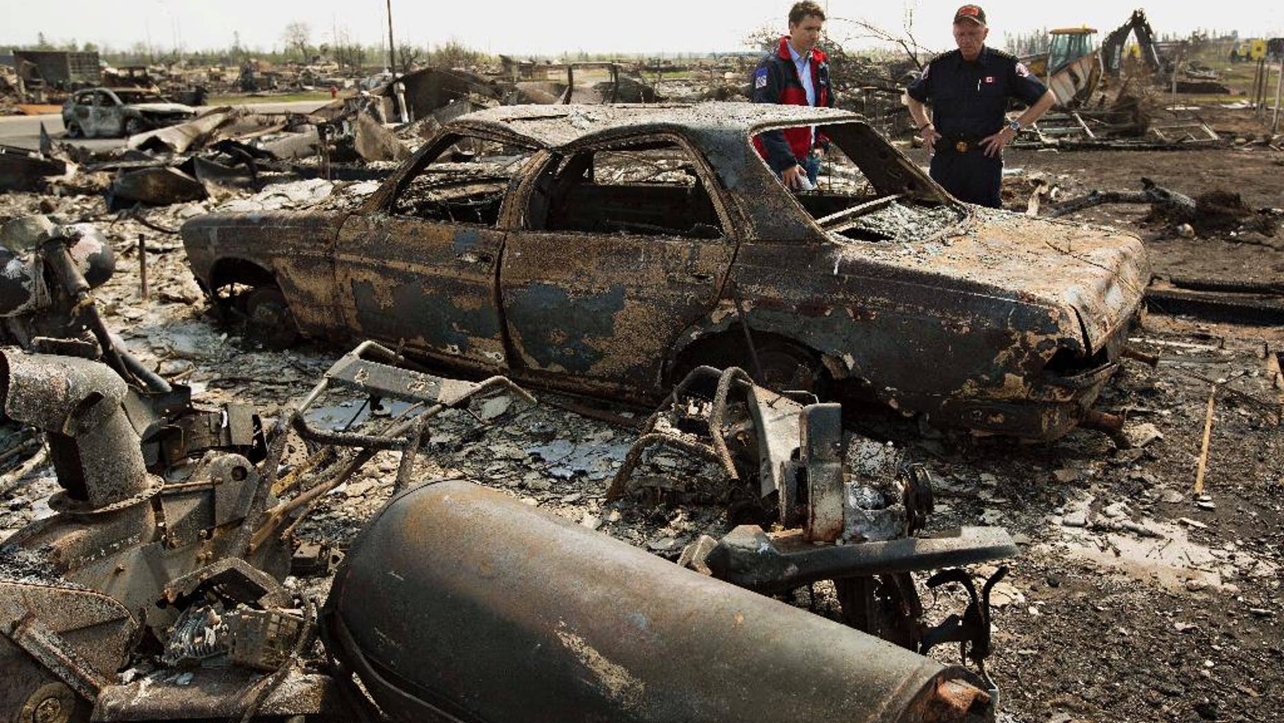 FILE - In this May 13, 2016 file photo, Canadian Prime Minister Justin Trudeau, left, and Fort McMurray Fire Chief Darby Allen look over a burnt out car during a visit to Fort McMurray, Canada. Canada's central bank says the Canadian economy will shrink and become much weaker than expected because of Alberta's devastating wildfires, which shut down its oil sands production. The Bank of Canada, which kept its key interest rate on hold Wednesday, May 25, said its preliminary assessment is that the destruction and halt to oil production will knock about 1 1/4 percentage points off real GDP growth in the second quarter.(Jason Franson/The Canadian Press via AP) MANDATORY CREDIT