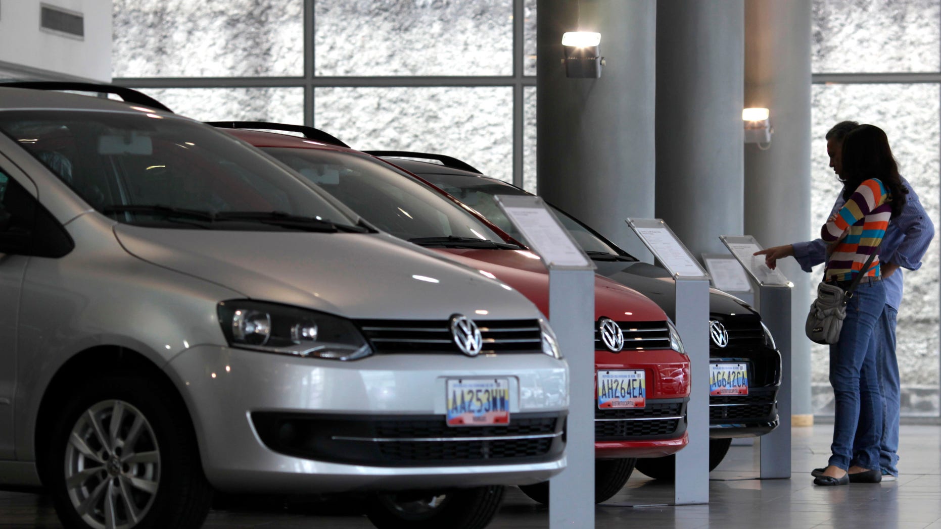 In this Feb. 1, 2013 photo, a couple looks at the price of a new vehicle that has already been sold, parked next to other already sold cars on display at a Volkswagen salesroom in Caracas, Venezuela. Venezuela may be the only country in the world where a new car becomes more expensive the instant it's driven off the dealership lot. The price reversal, many economists say, is the result of President Hugo Chavez’s socialist-oriented economic controls. New cars have become so scarce that many showrooms sit nearly empty and would-be buyers must sign up on long waiting lists. (AP Photo/Ariana Cubillos)