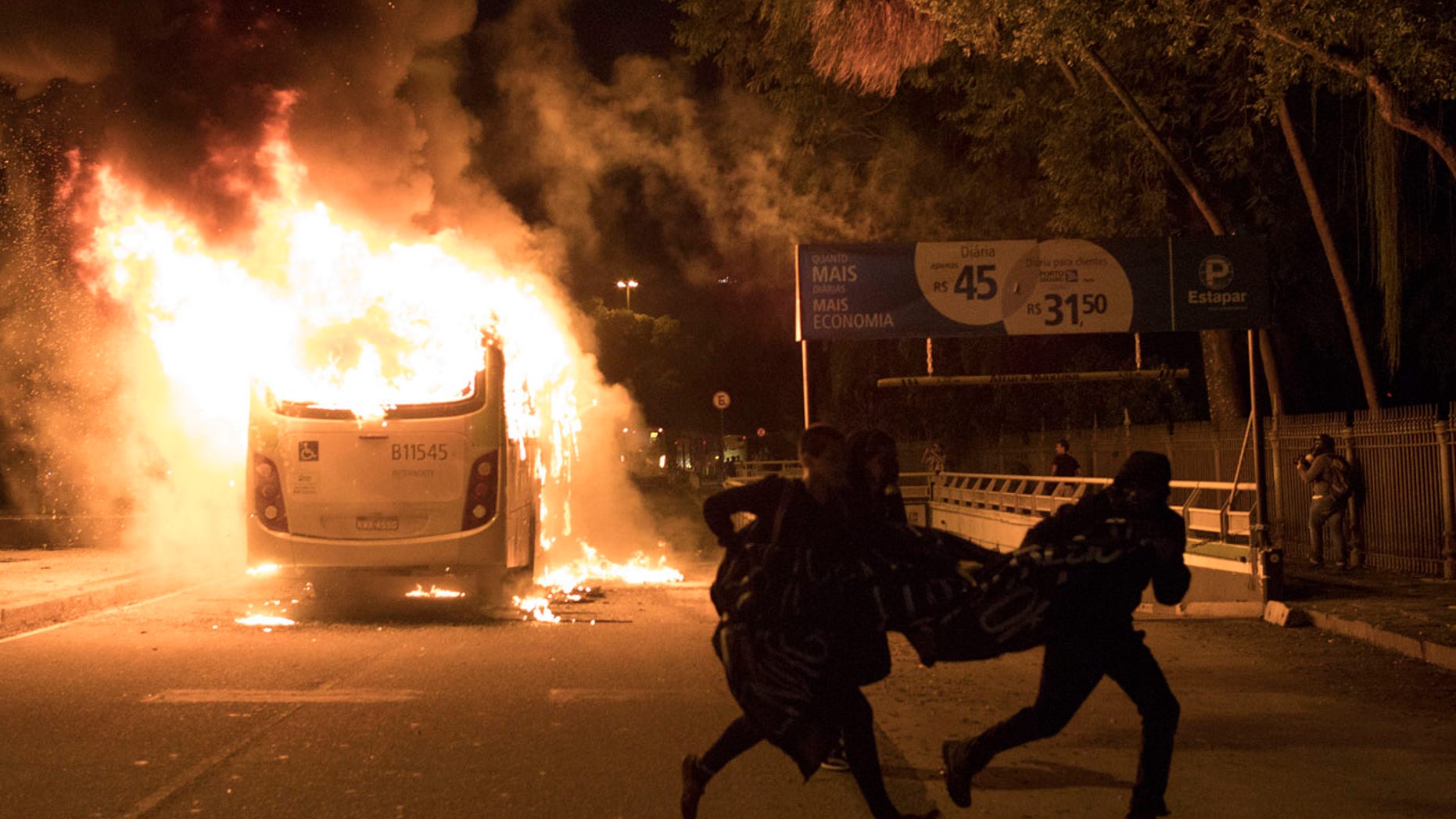 Demonstrators run past a bus set fire by protesters during a general strike protest in Rio de Janeiro, Brazil, Friday, April, 28, 2017